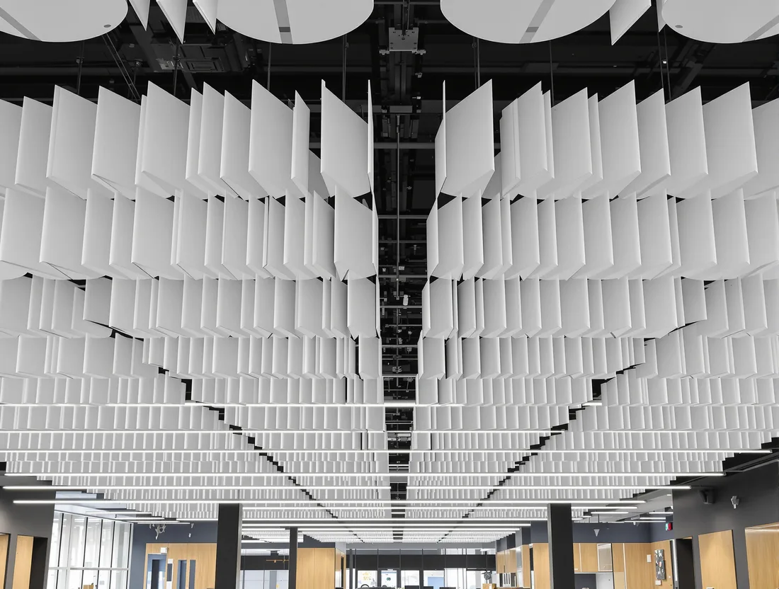 Rows of vertical white acoustic baffles hung beneath a blacked-out open ceiling, with linear lighting suspended between them.