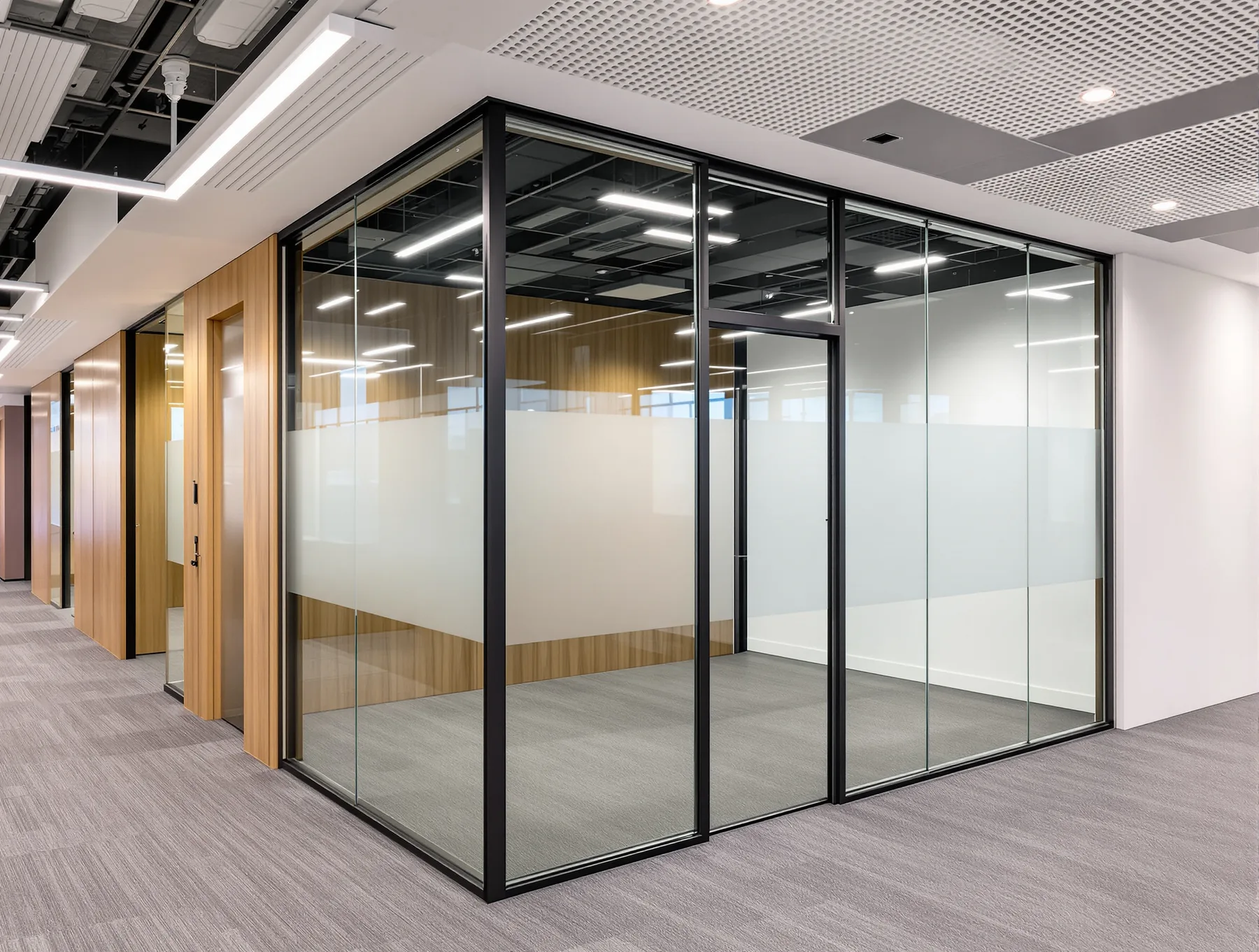 A framed glass meeting room in a commercial office, showing the head track at the ceiling, the base channel at the carpet and a frosted manifestation band at eye height.
