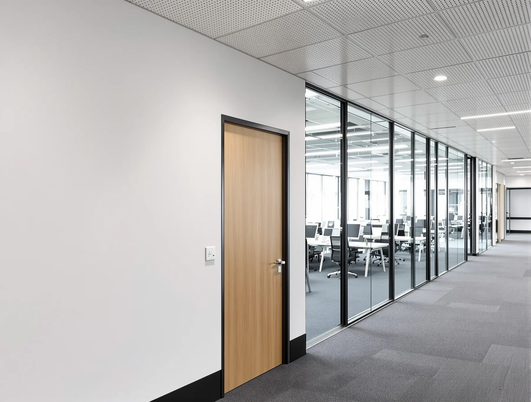 A plasterboard return with a timber door meeting a black-framed glass partition, with the suspended ceiling grid running over both.