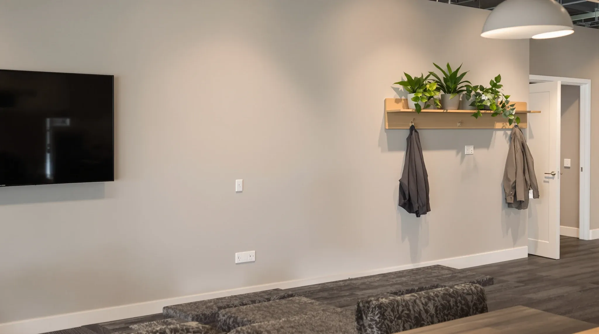 A painted plasterboard office wall carrying a dark screen, shelving, hooks and outlets in the evening