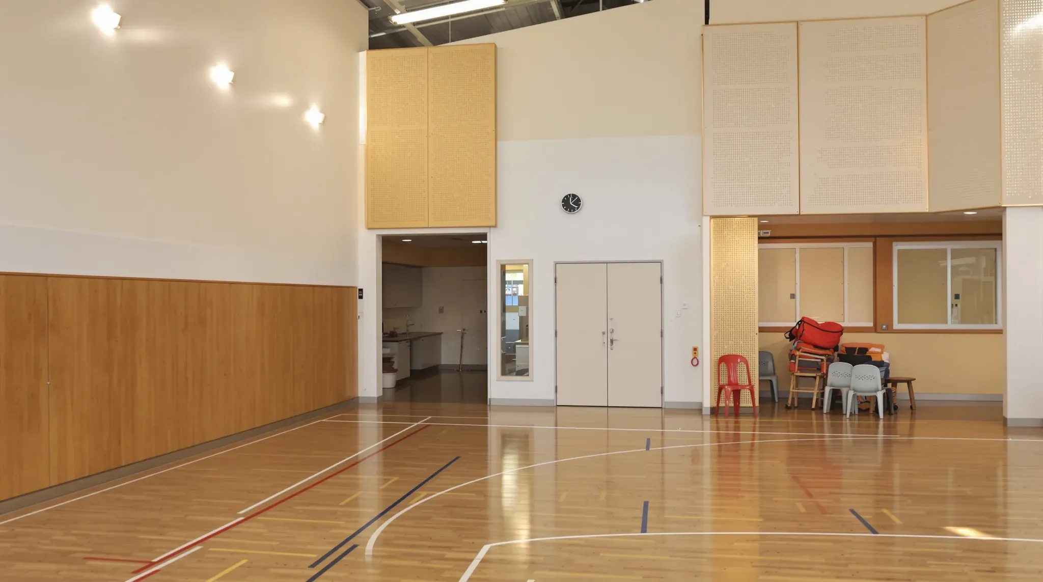 School hall with timber wall lining and acoustic panels, a kitchenette doorway, a store and an office window
