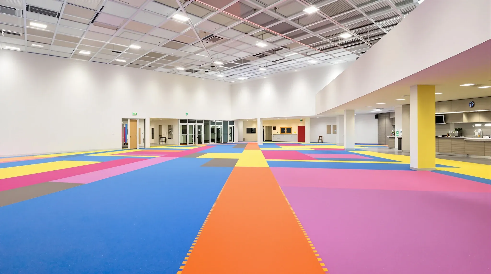 Empty finished play centre hall with high ceiling, colourful soft floor zones, cafe counter edge, no branding