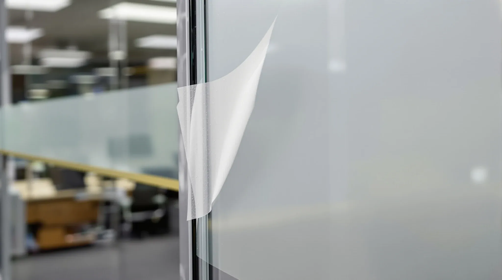 Close detail of old frosting film lifting and bubbling at the edge of an office glass panel