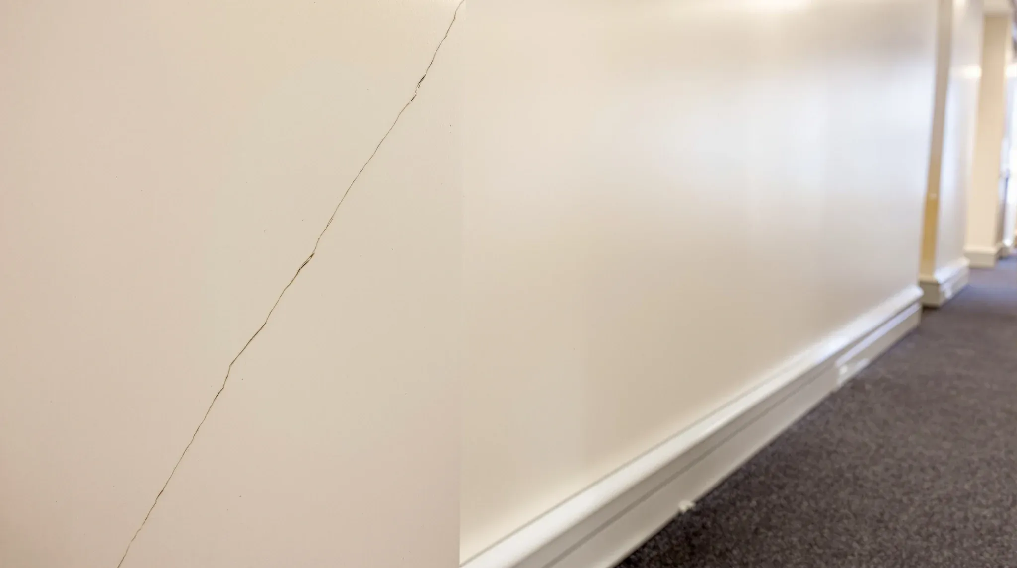 A hairline crack running up from a door frame corner in a painted office corridor wall
