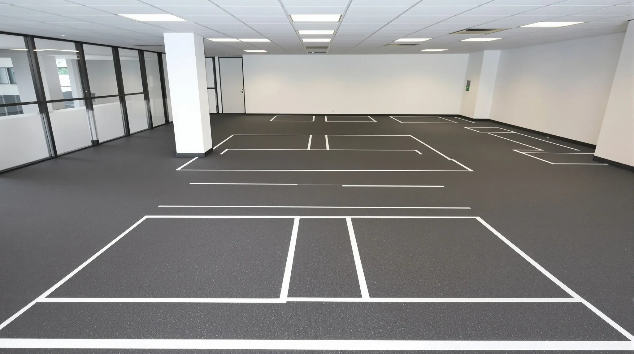 A vacant office floor with white tape on the carpet marking two rows of desks and a meeting room