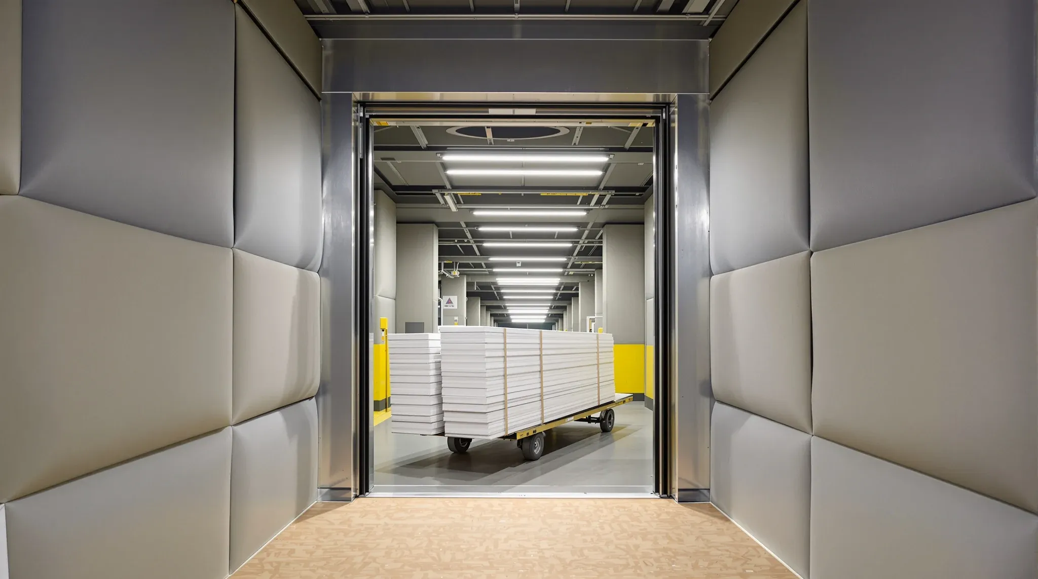 Plasterboard sheets on a trolley waiting outside a goods lift lined with padded blankets