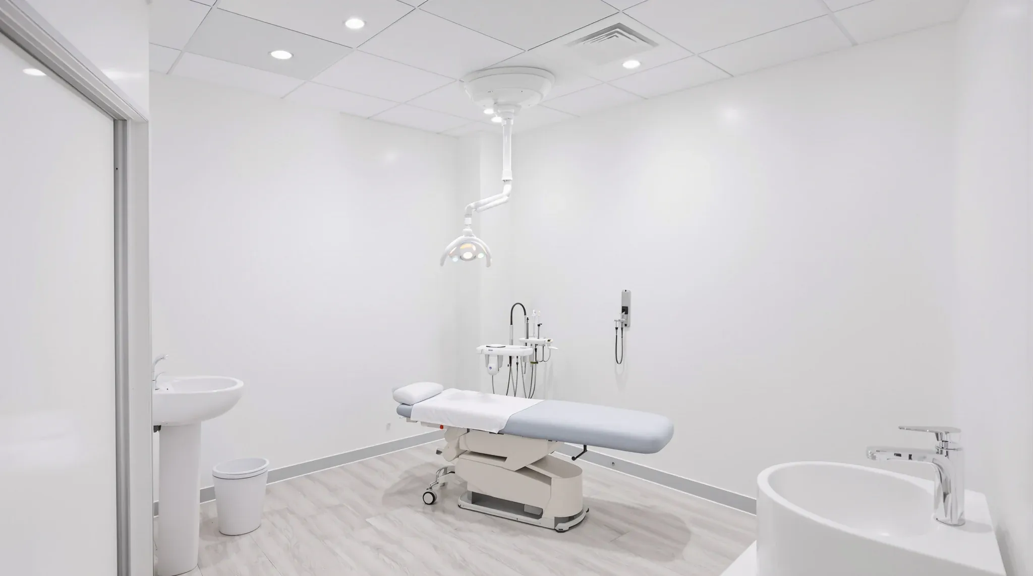 Empty finished examination room with bright white lighting, treatment couch, basin