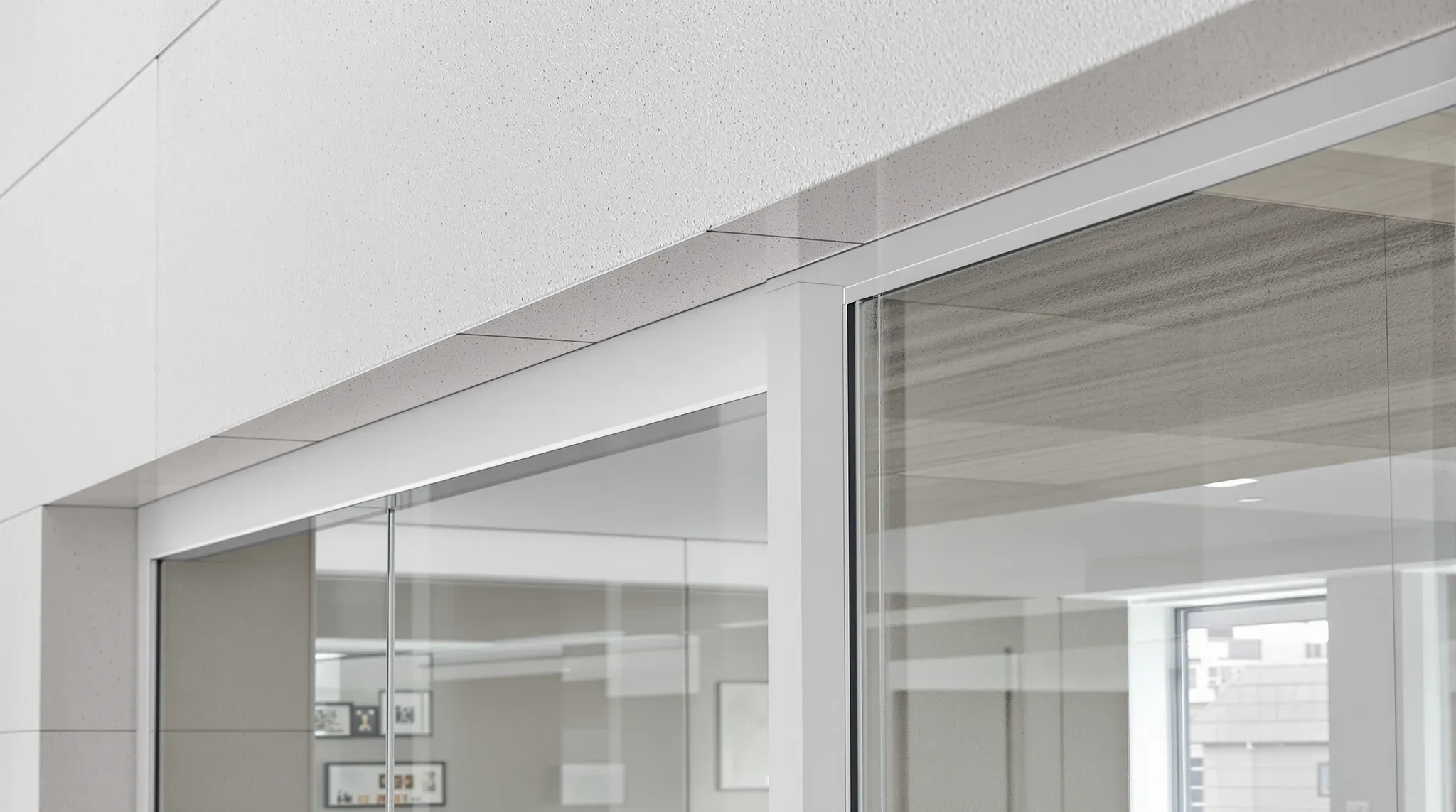 The top of a glass partition meeting a plasterboard bulkhead beside a window mullion