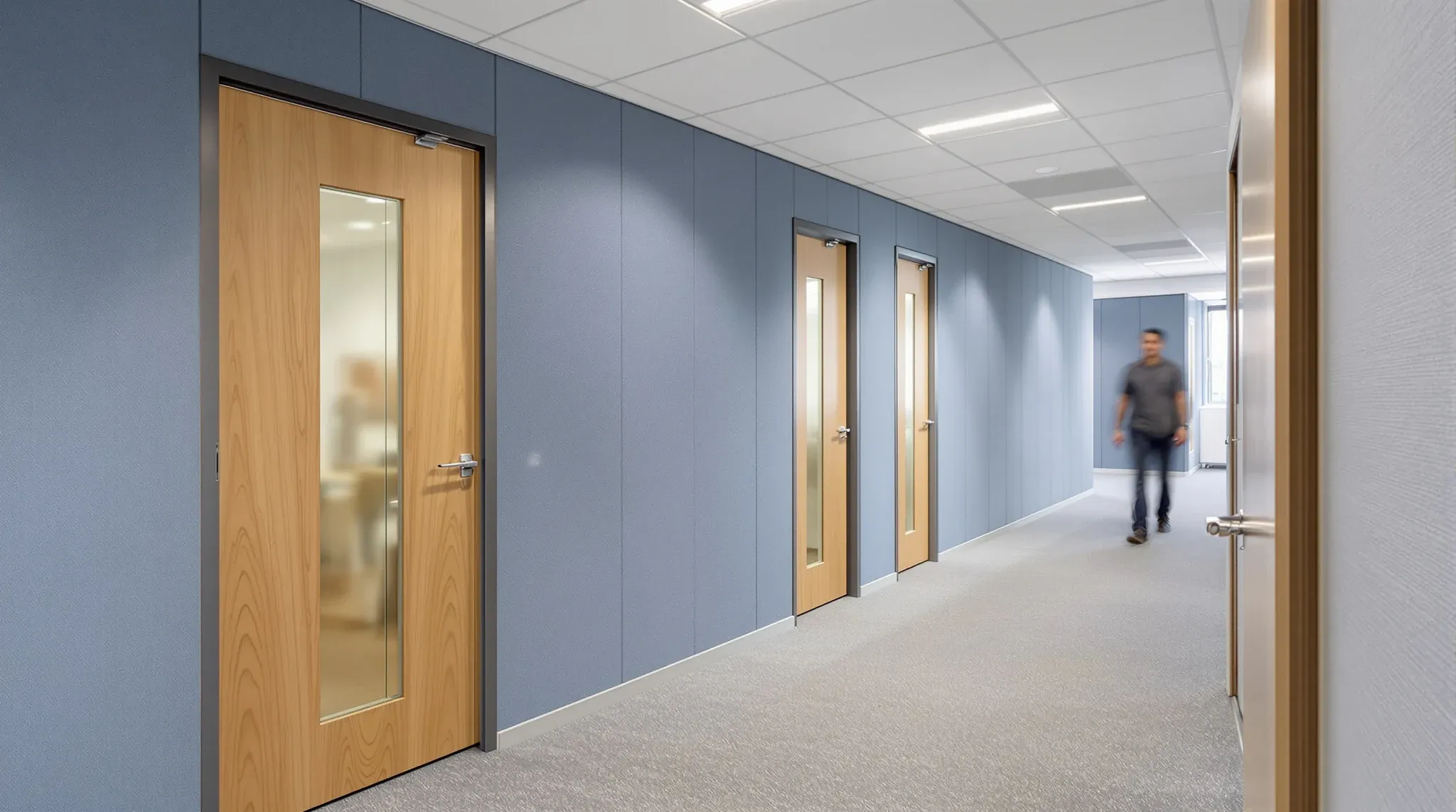 A corridor of small focus rooms with oak doors and blue felt acoustic wall panels
