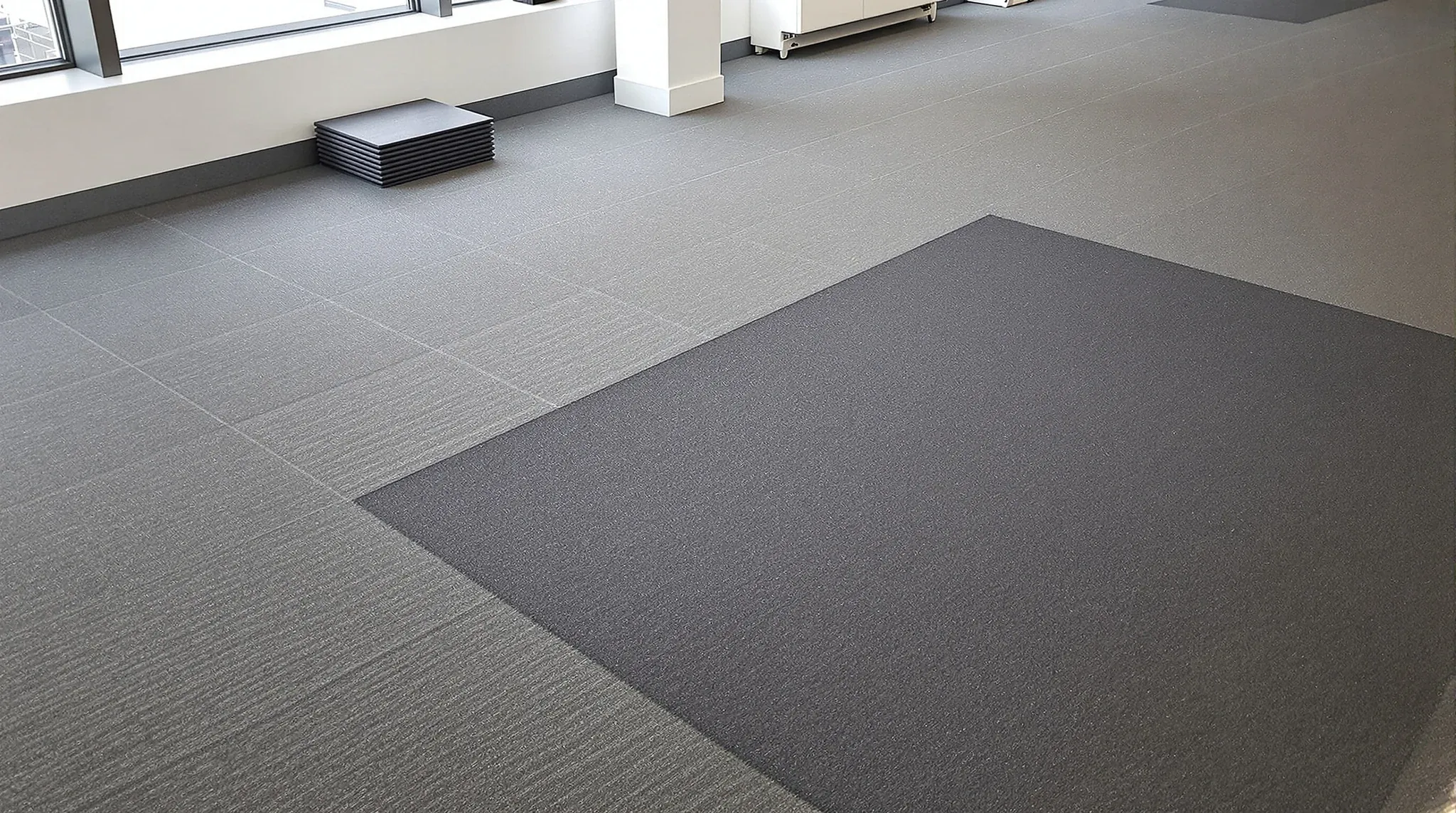 A commercial carpet tile floor with a patch of newer replacement tiles near the window