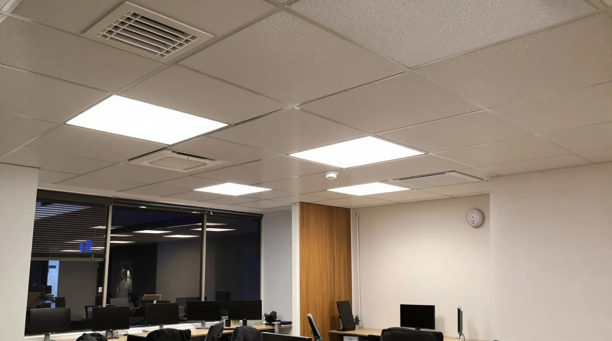 A compact office with air vents, lights, sprinkler heads and a smoke detector crowded into a low ceiling