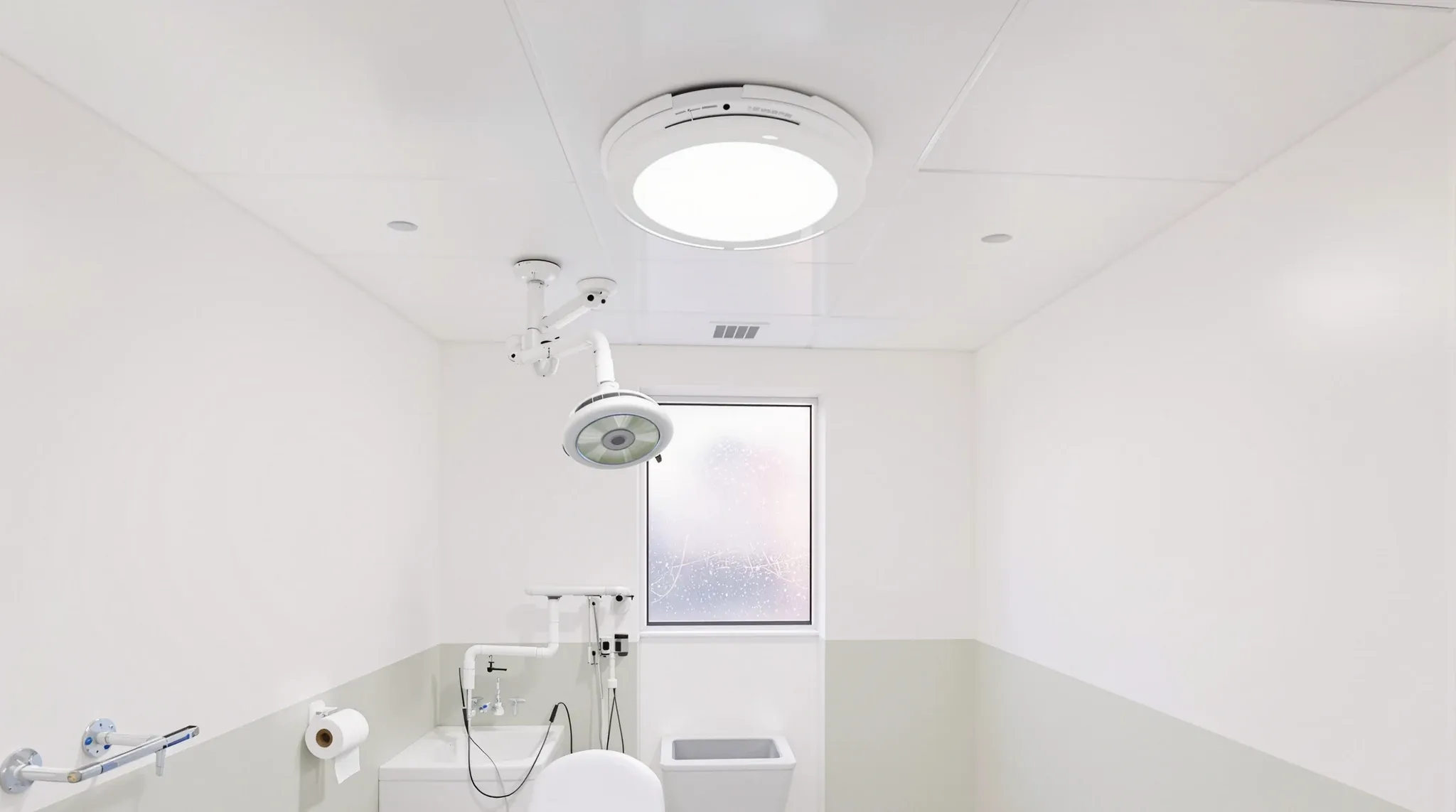 A sealed hygienic ceiling with a flush light and examination lamp above a treatment couch