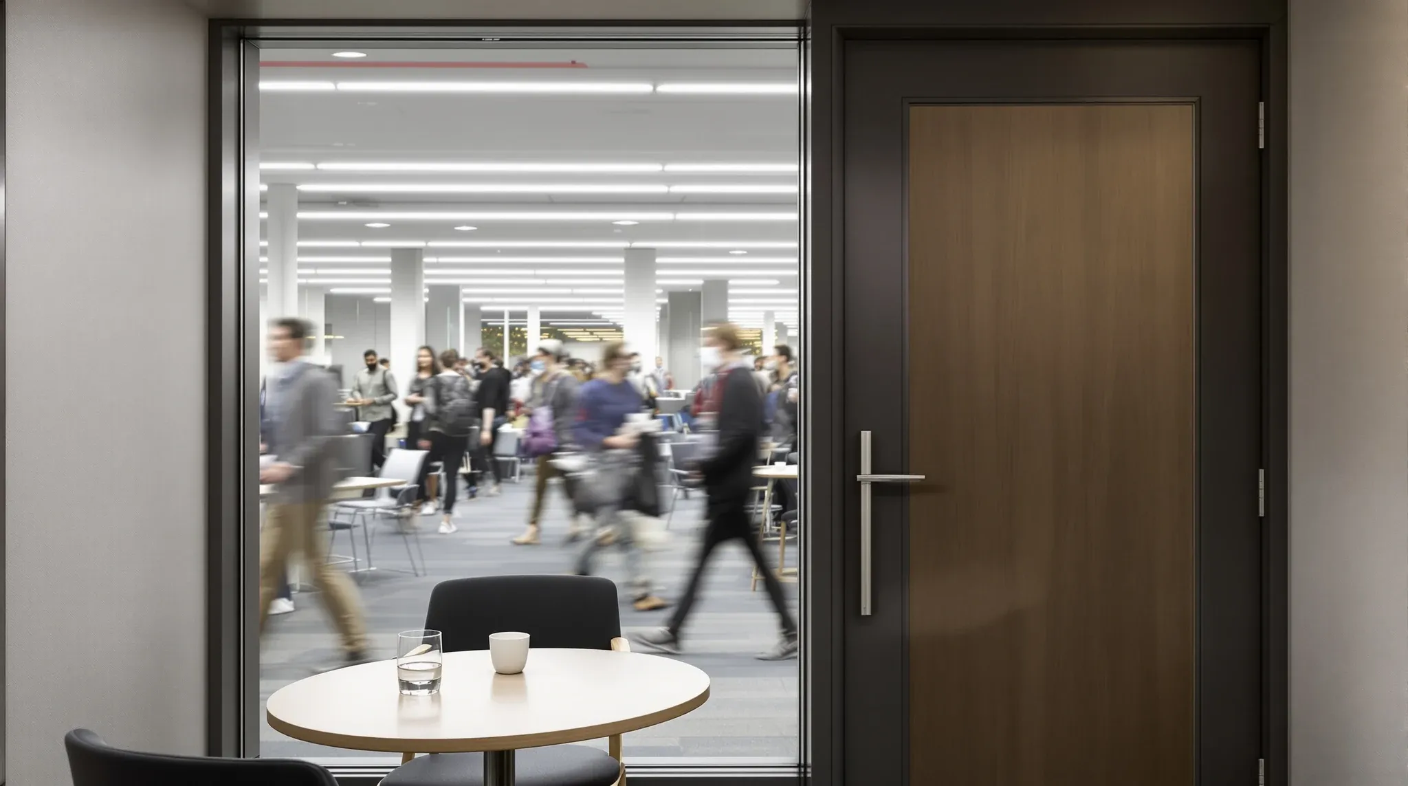 View from inside a small interview room out through a deep double-glazed front to a busy office