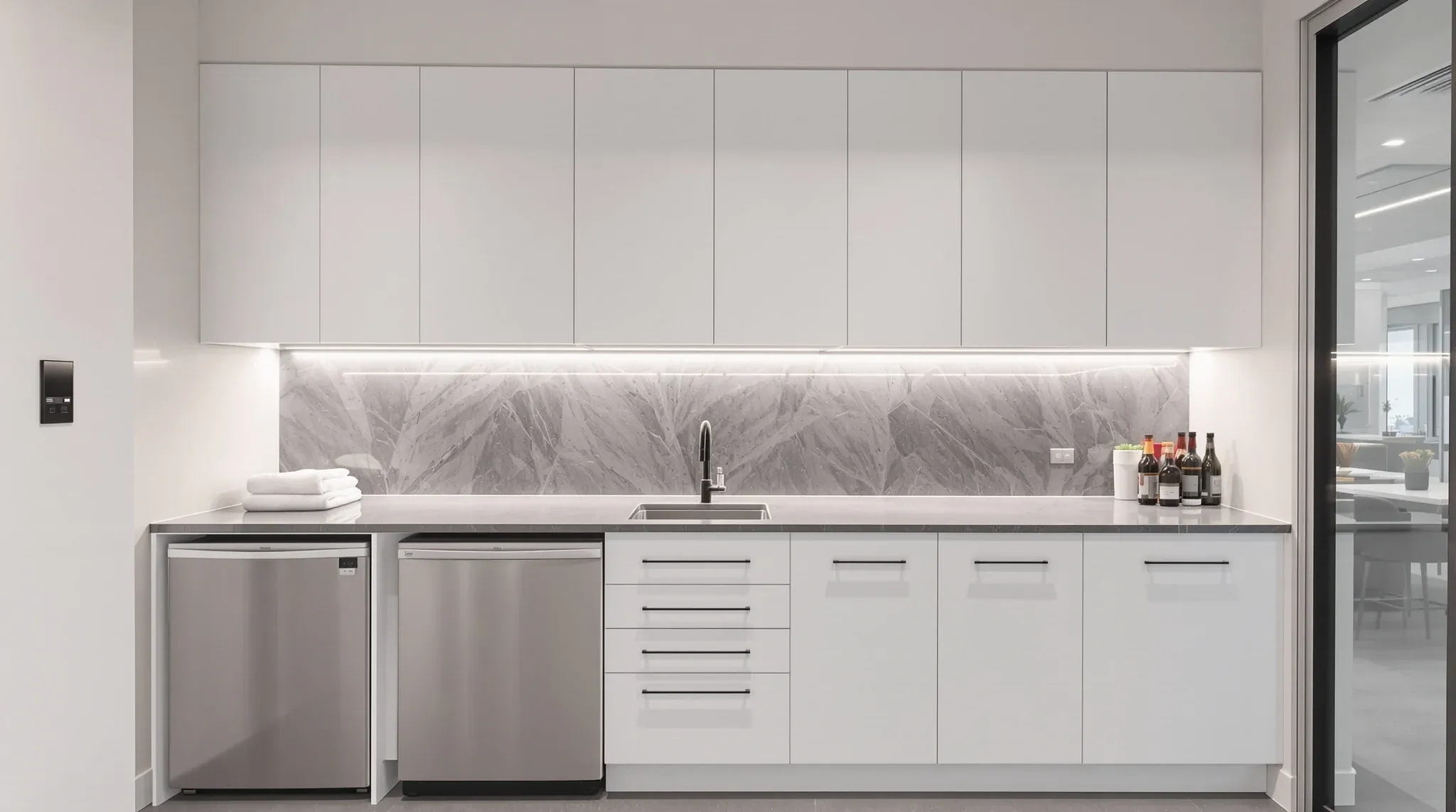 A small office tea point with white cupboards, a stone bench, a sink and a boiling water tap