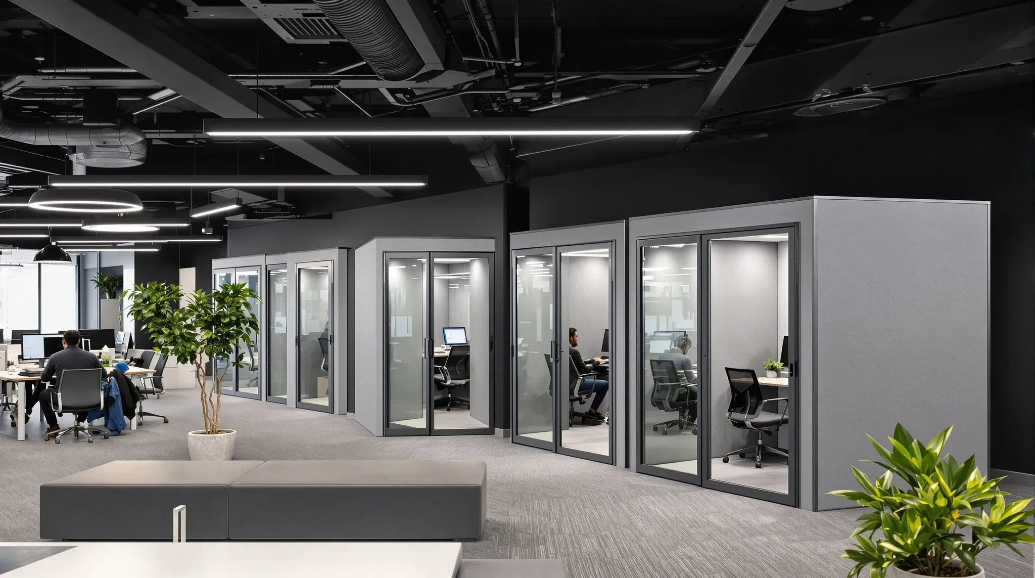 A working tech office with bench desks, plain grey felt phone booths and a black exposed ceiling