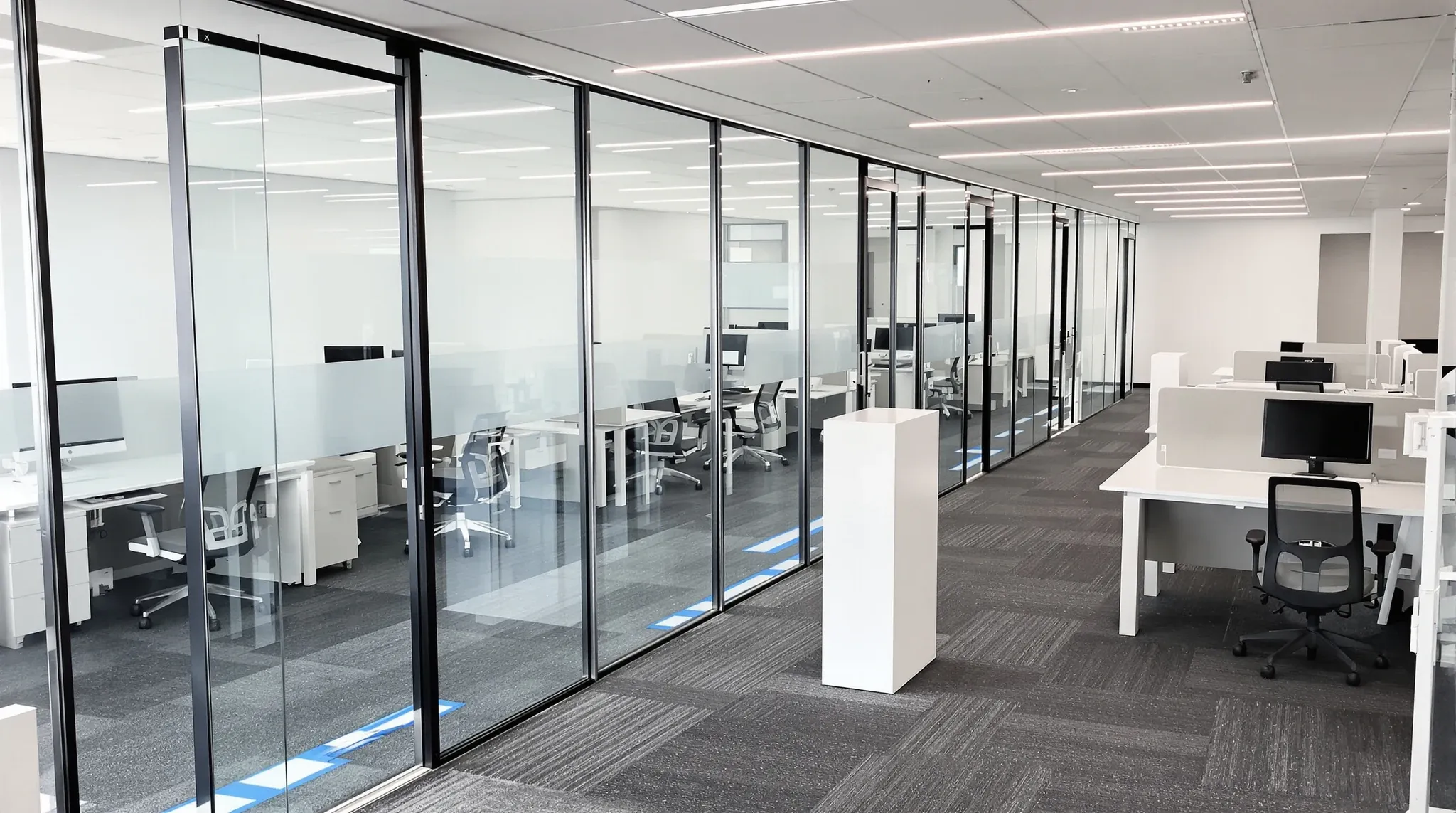 A new glass partition with protective film still on it beside desks covered in plastic on a quiet weekend