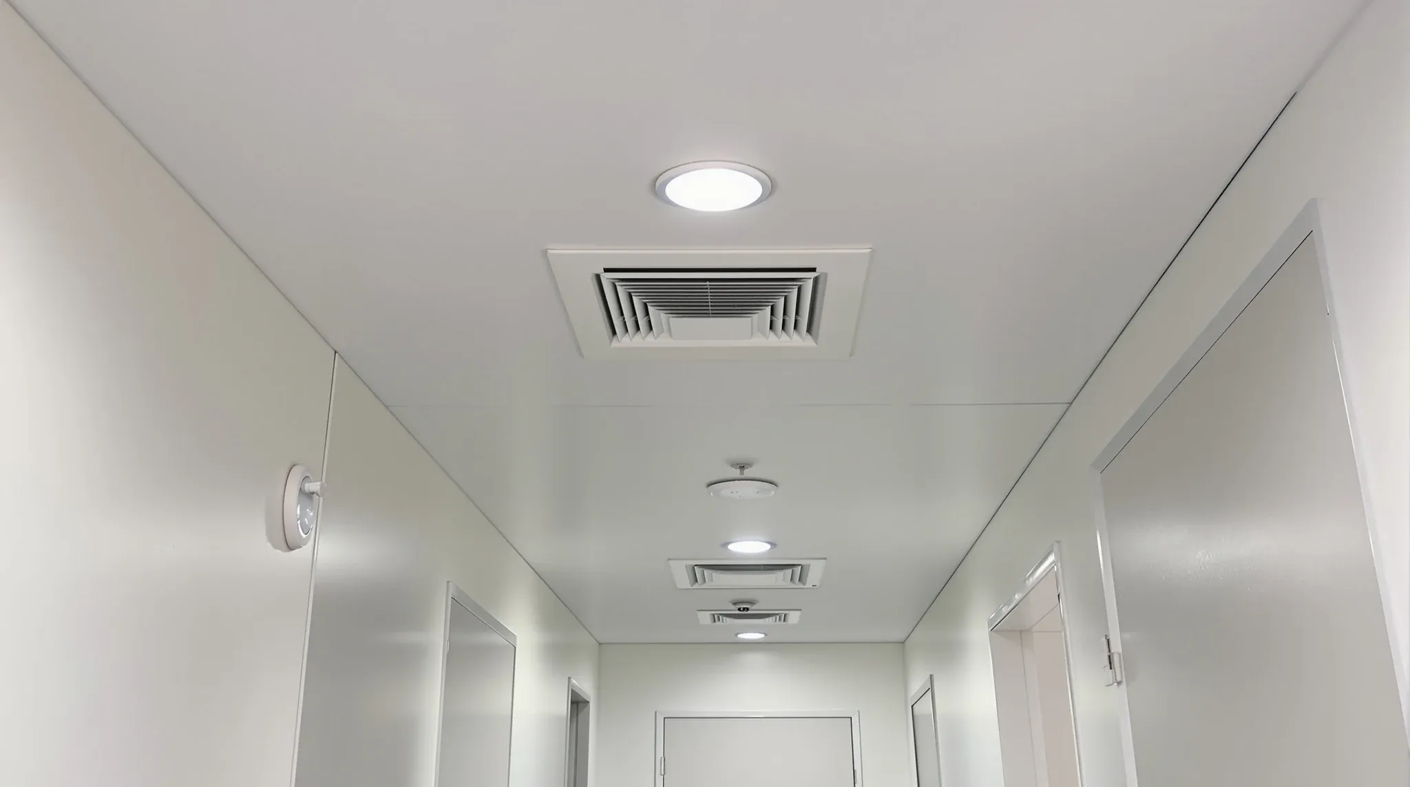 A smooth plasterboard corridor ceiling with a flush access panel, sprinkler and emergency light