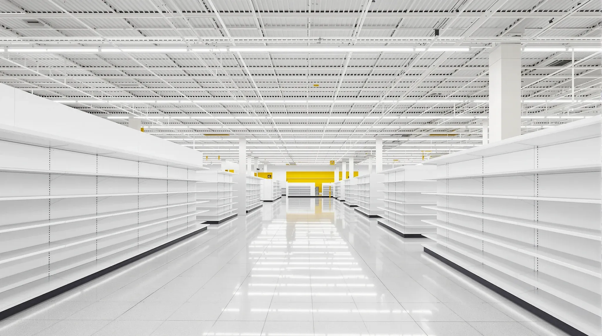 Empty finished large retail floor with long aisles of empty white shelving, bright grid ceiling, no branding