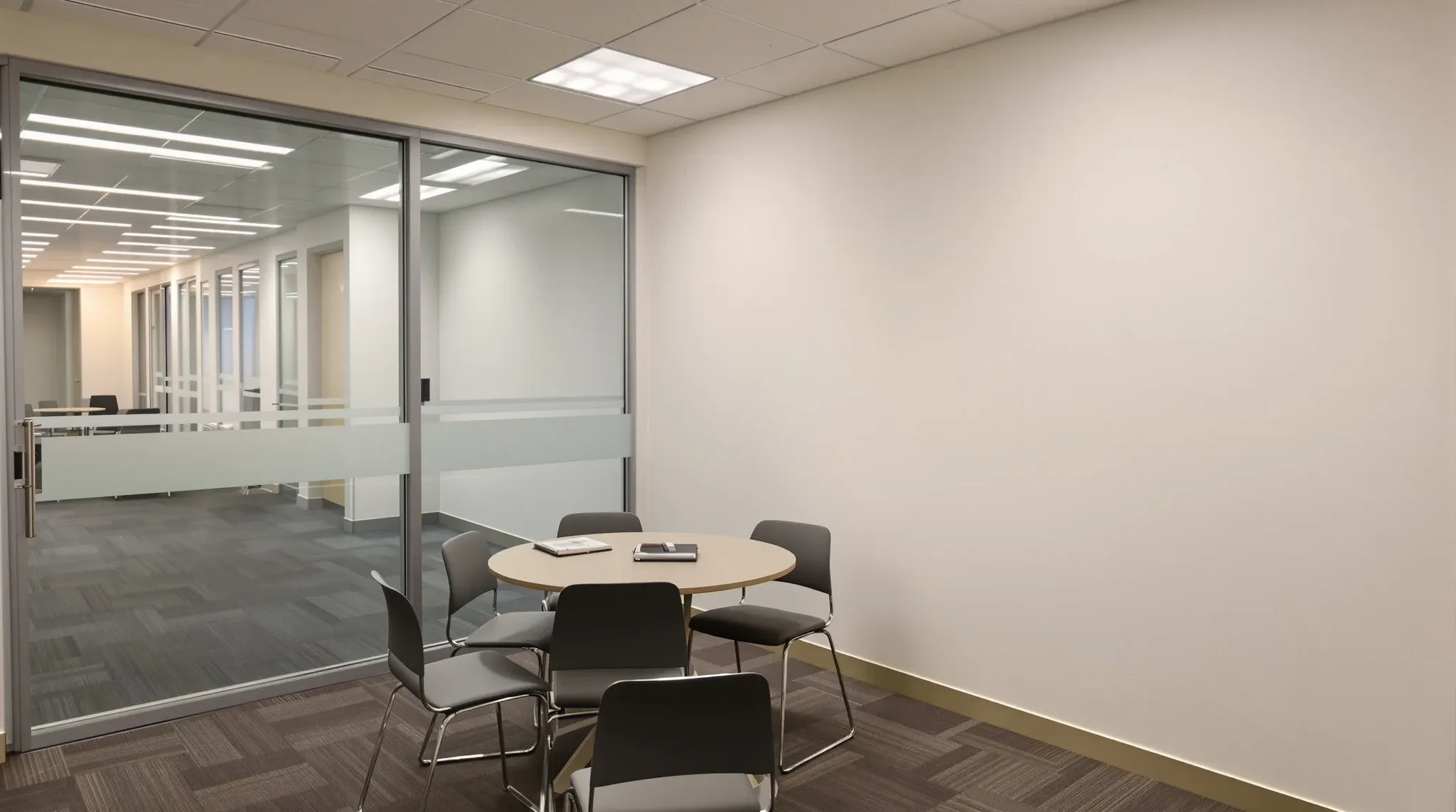 Small tutoring room with a table, chairs, whiteboard wall and a glazed door with a frosted band opening onto a corridor