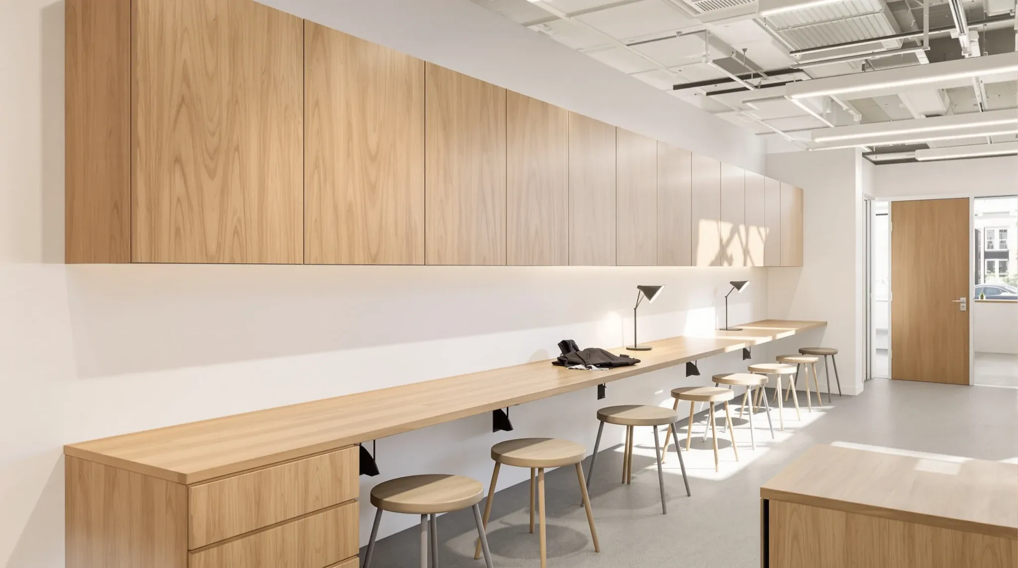 A long oak bench desk and wall cupboards fixed along a painted plasterboard wall in an office project room