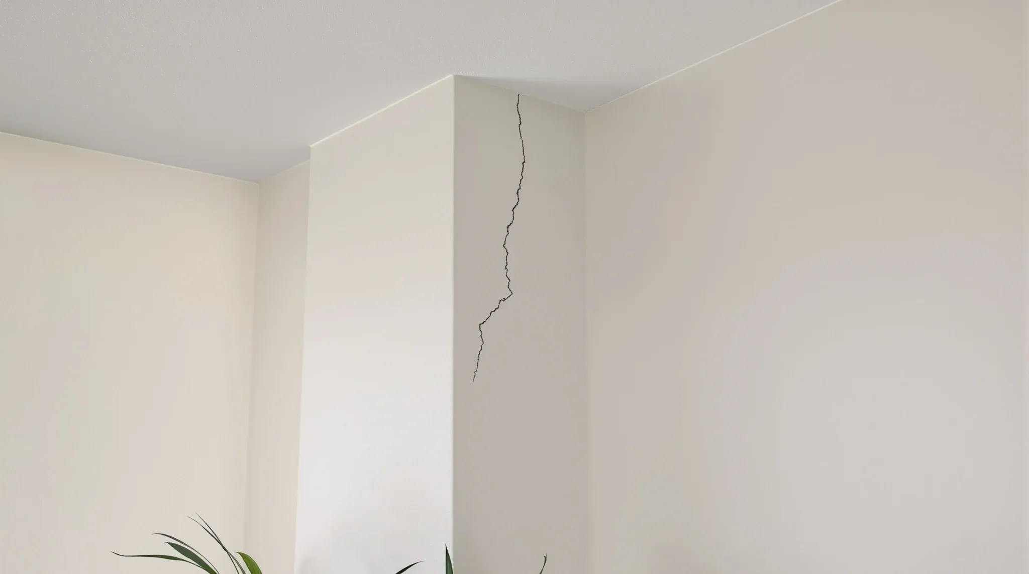 A fine hairline crack running down from the ceiling corner of a painted office wall in side light