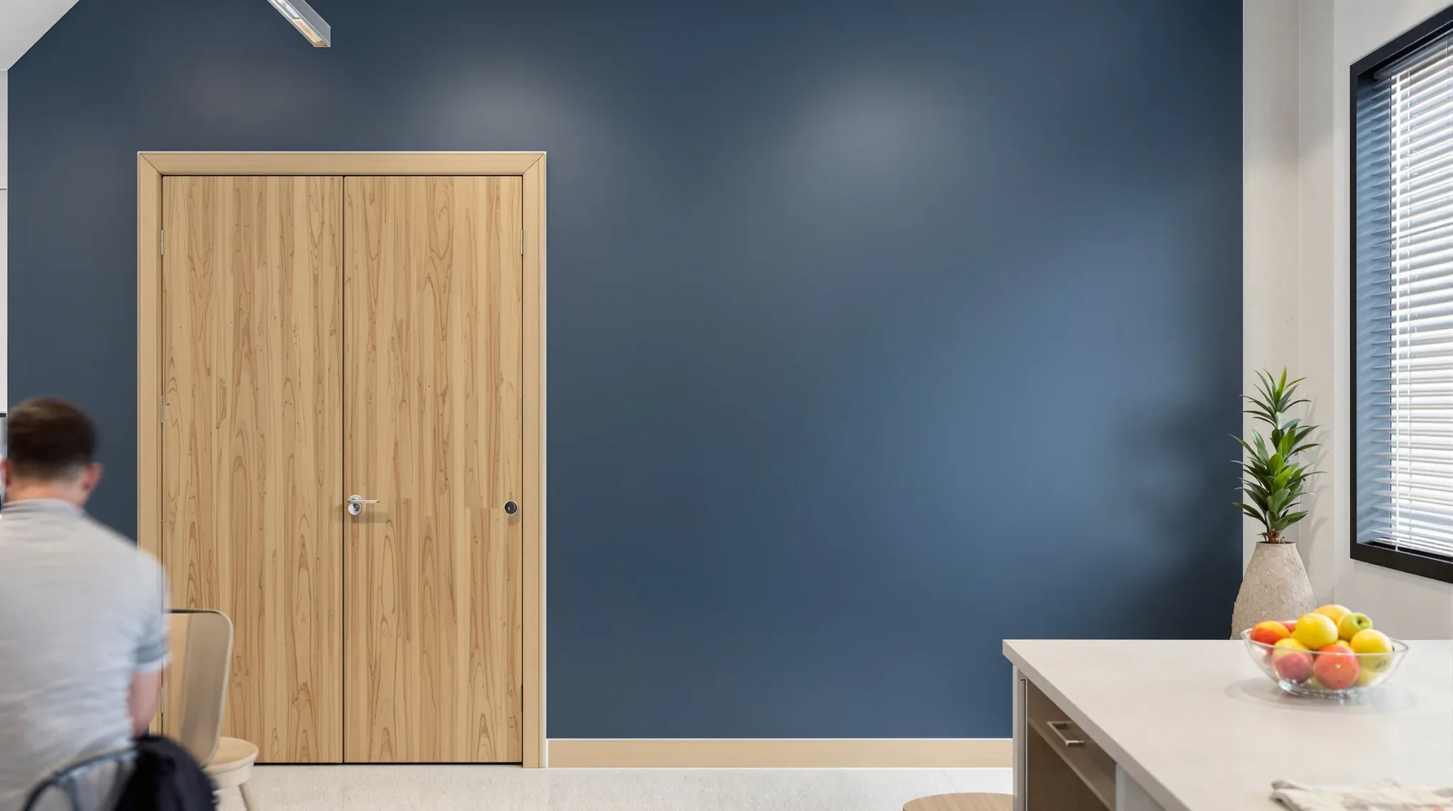 A solid painted boardroom wall with a heavy closed door beside a busy staff kitchen