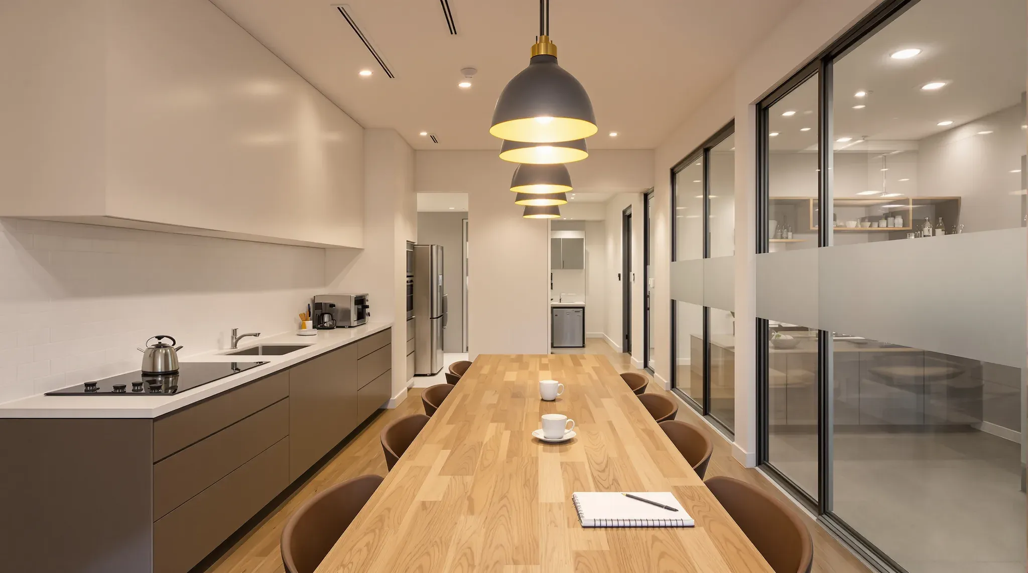 Student residence common room with a shared kitchen, a long timber table and a glass-fronted study room