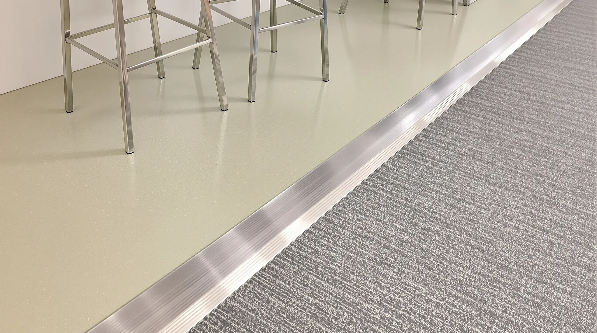 Sheet vinyl in an office kitchen meeting carpet tiles at a thin metal transition strip