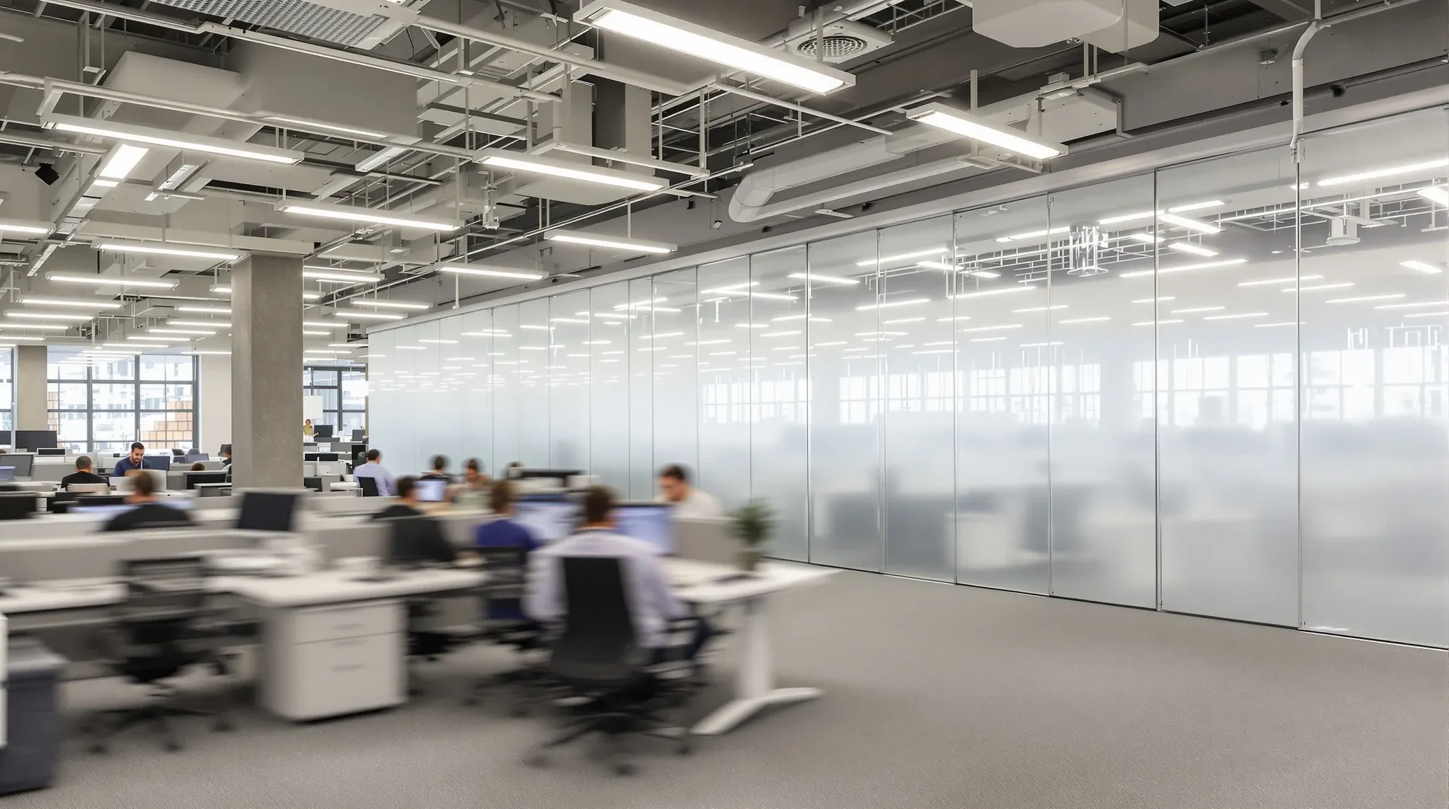 An occupied office working normally while a ceiling zone at the far end is screened off