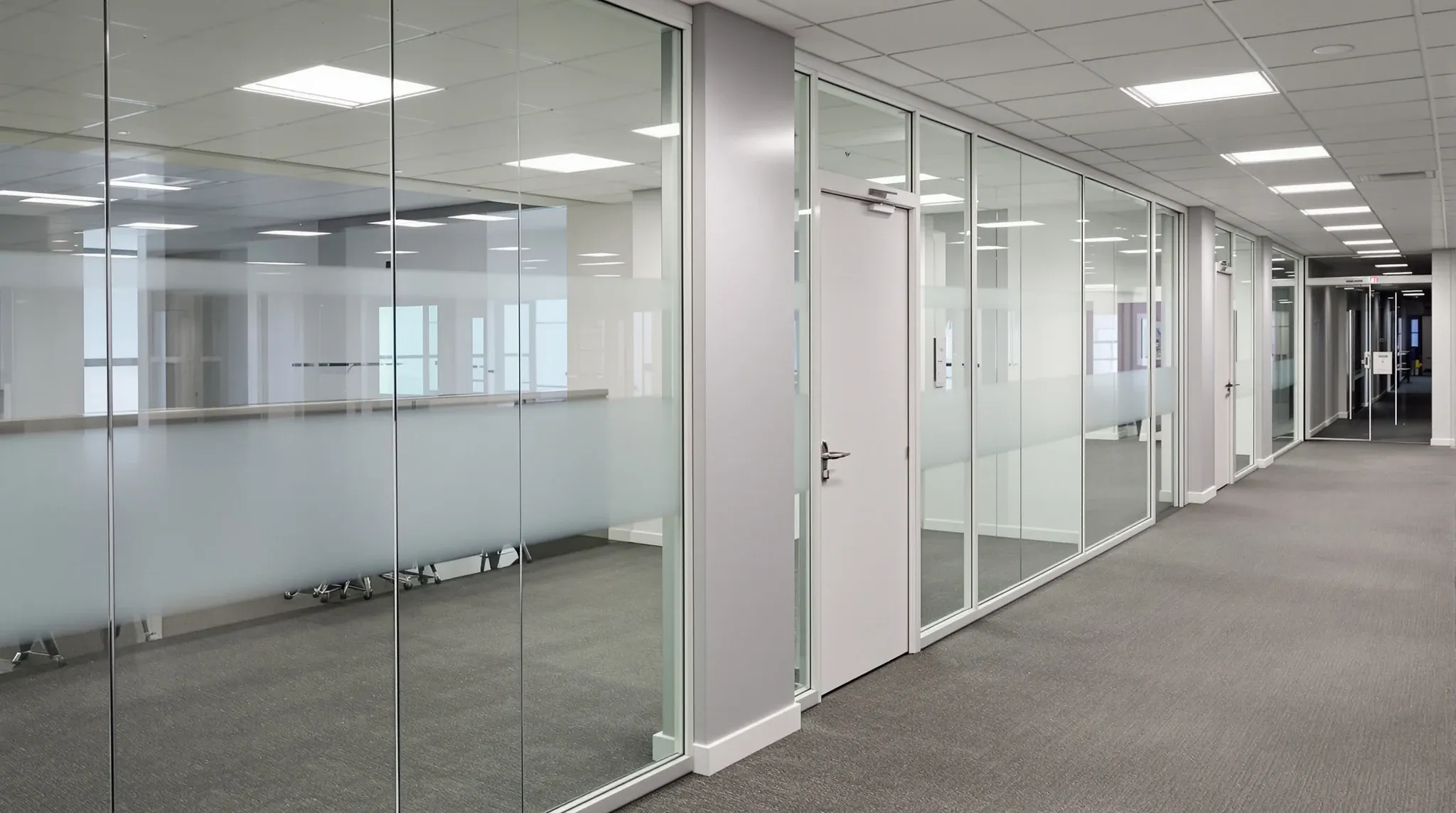 A glass partition wall beside a plain closed fire stair door in an office corridor