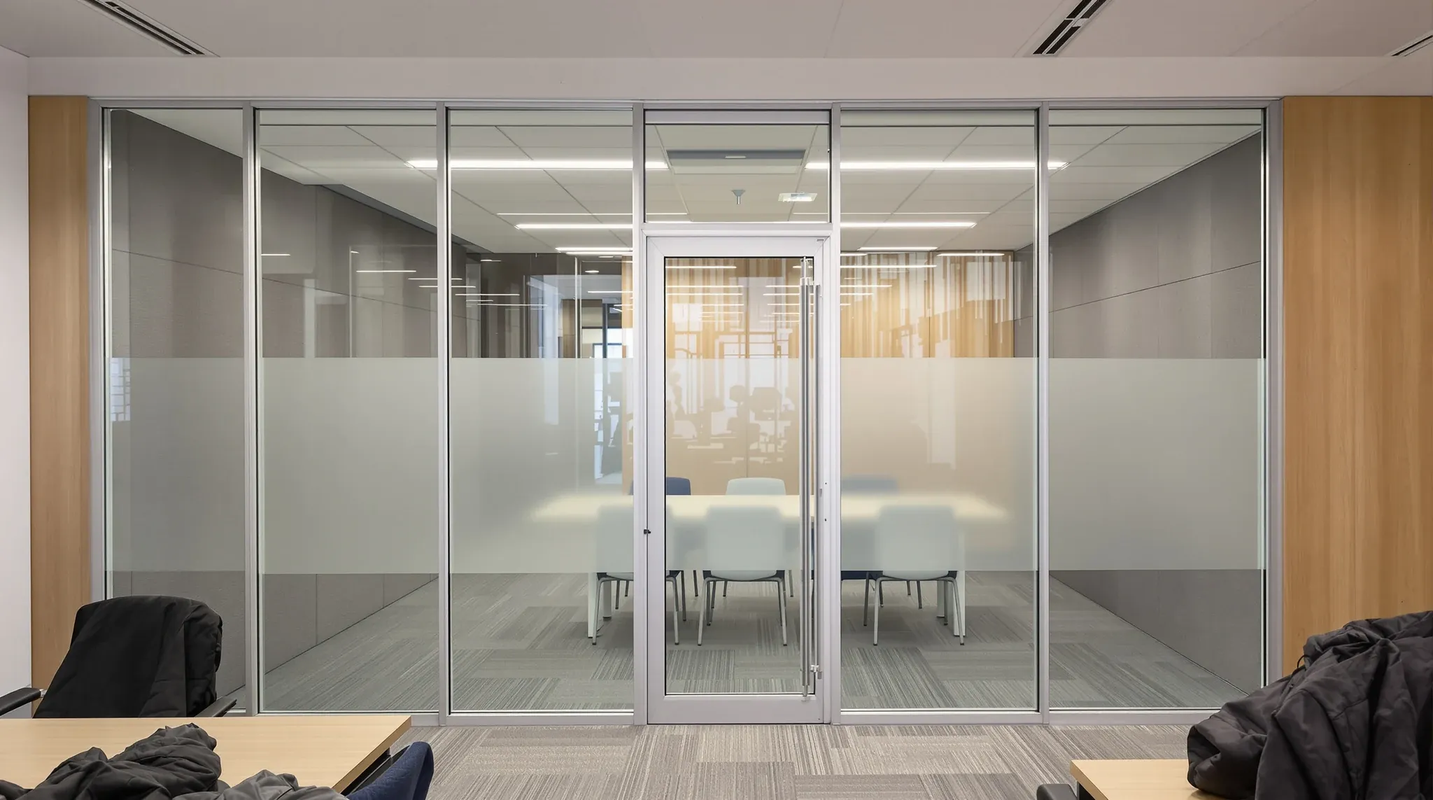 A silver-framed glass meeting room with a frosted band and grey acoustic panels lining its walls