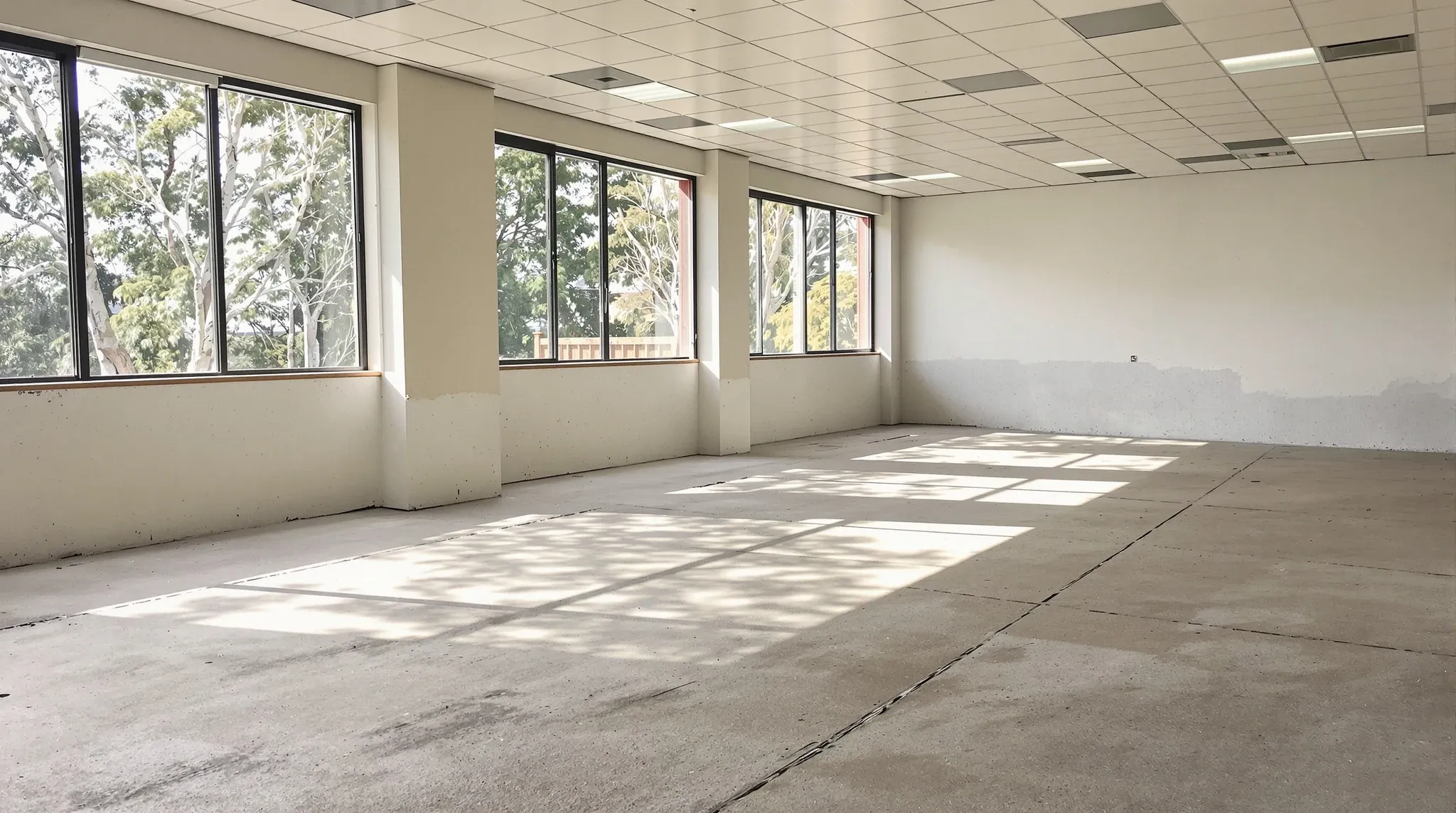 A stripped office tenancy with a bare swept concrete floor lit by late afternoon sun