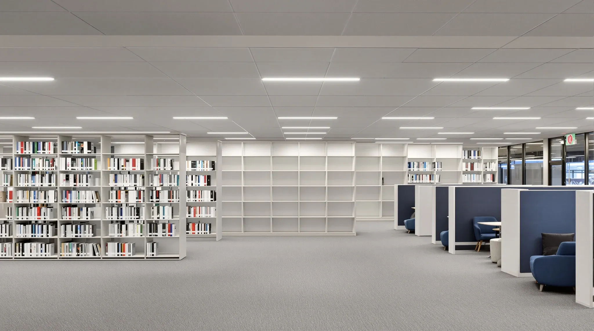 Empty finished library reading area with tall shelving (no book titles legible), study pods, acoustic ceiling