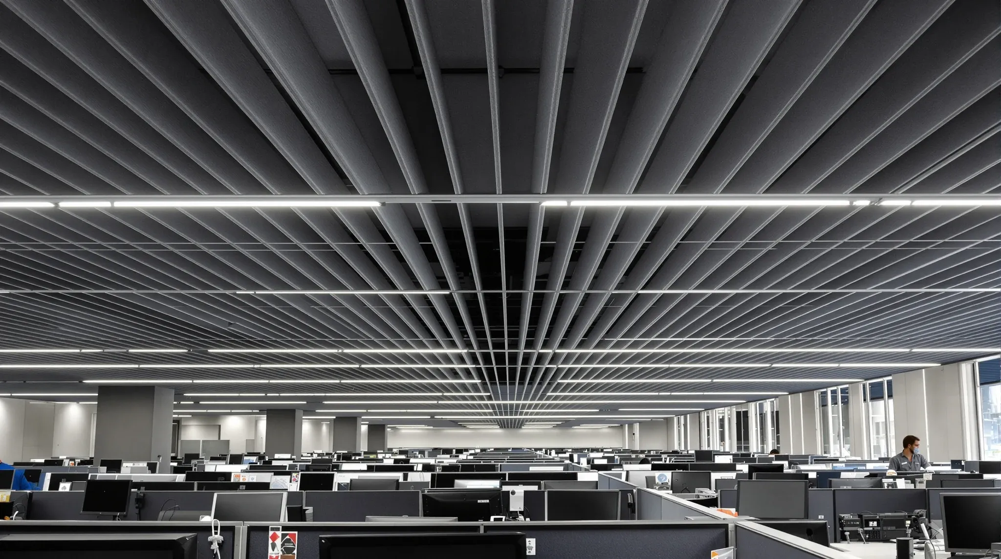 A call centre floor before a shift, rows of desks with headsets under a dark acoustic ceiling with felt baffles