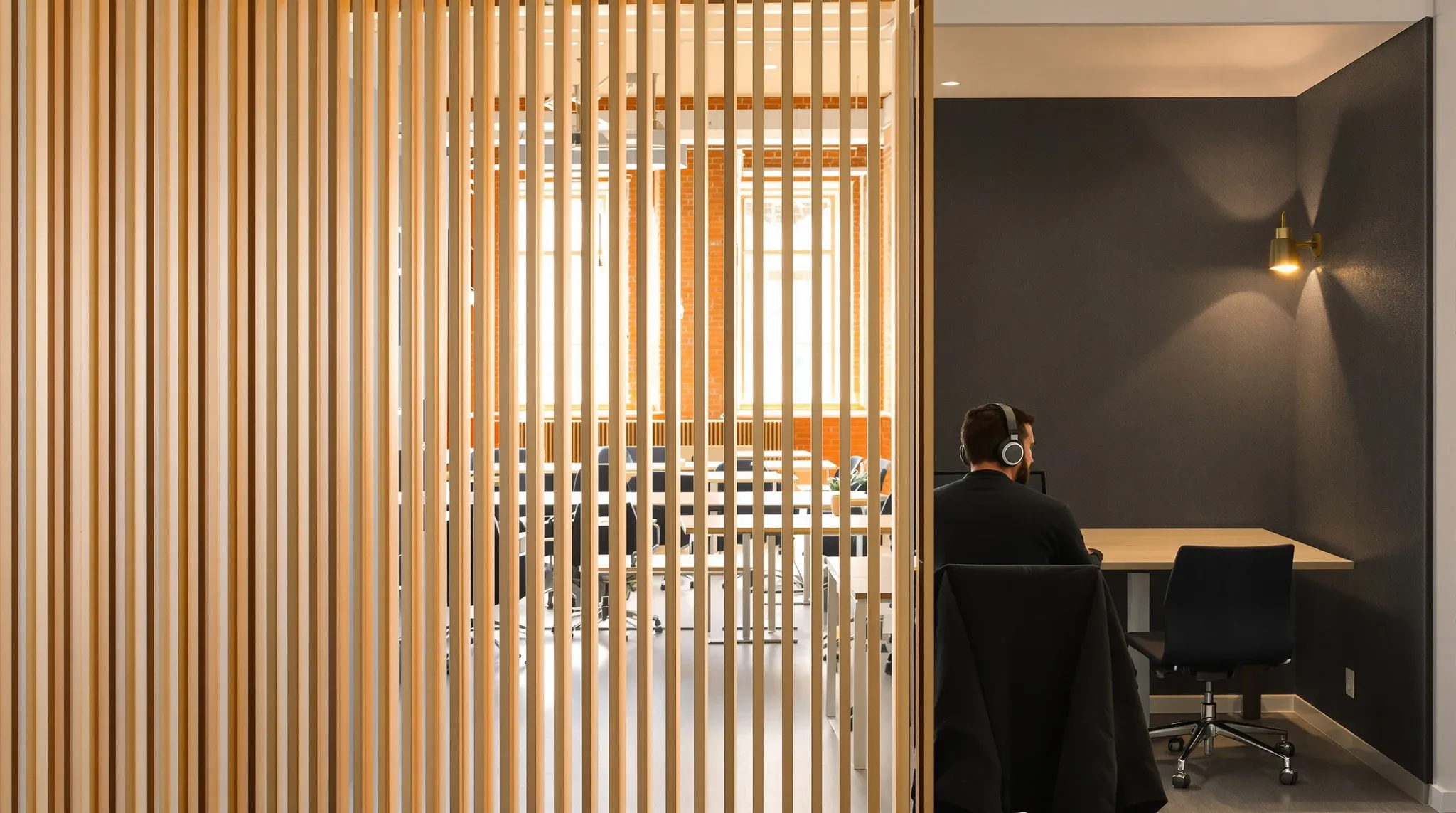 A person working alone in a quiet desk nook screened by a timber slat partition in early morning light
