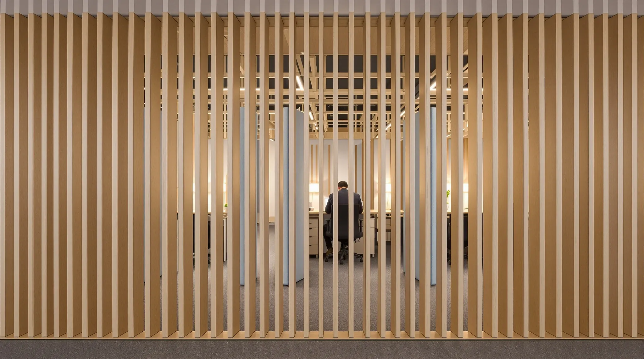 Desks with tall upholstered screens in a quiet focus zone, seen through timber slats