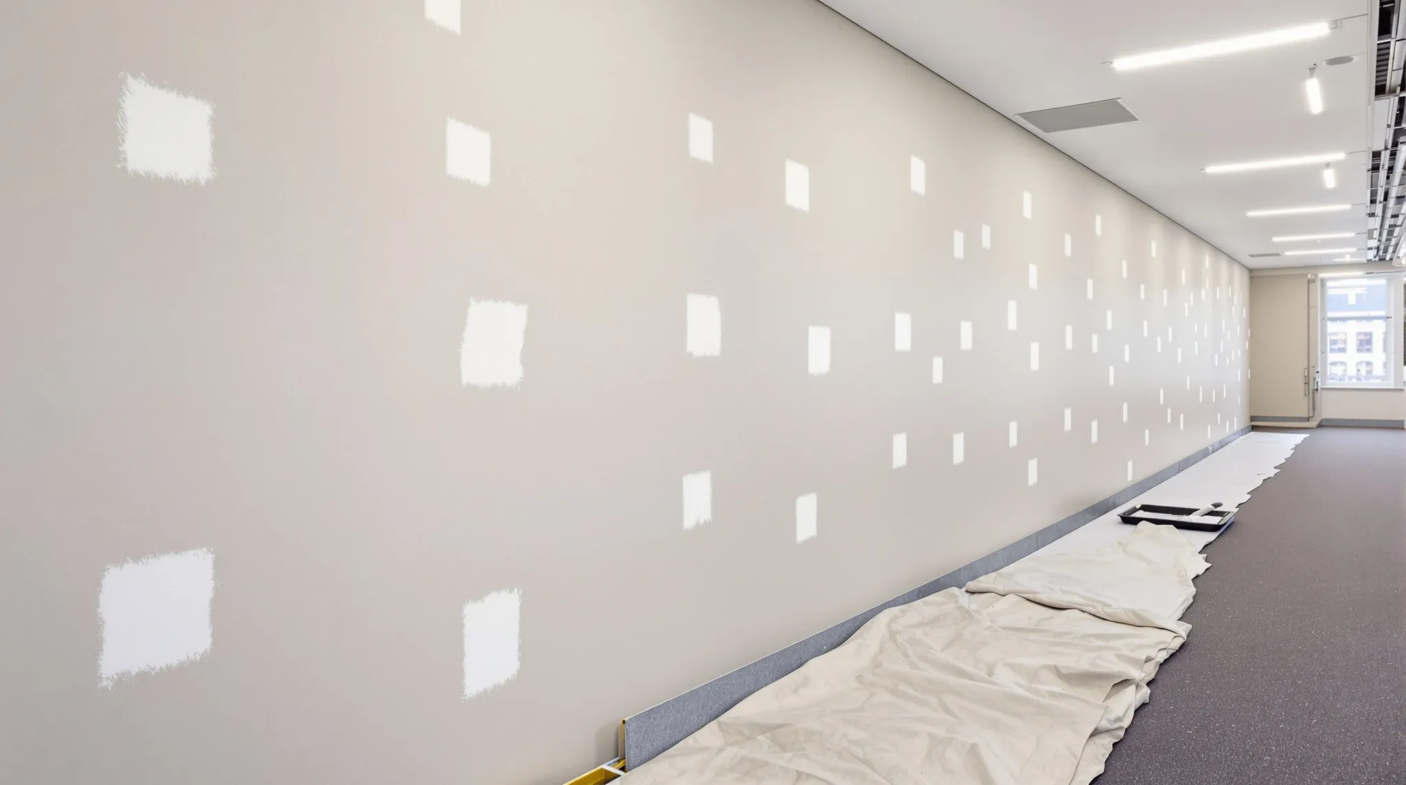Spot patches of fresh paint showing as brighter squares along an office wall