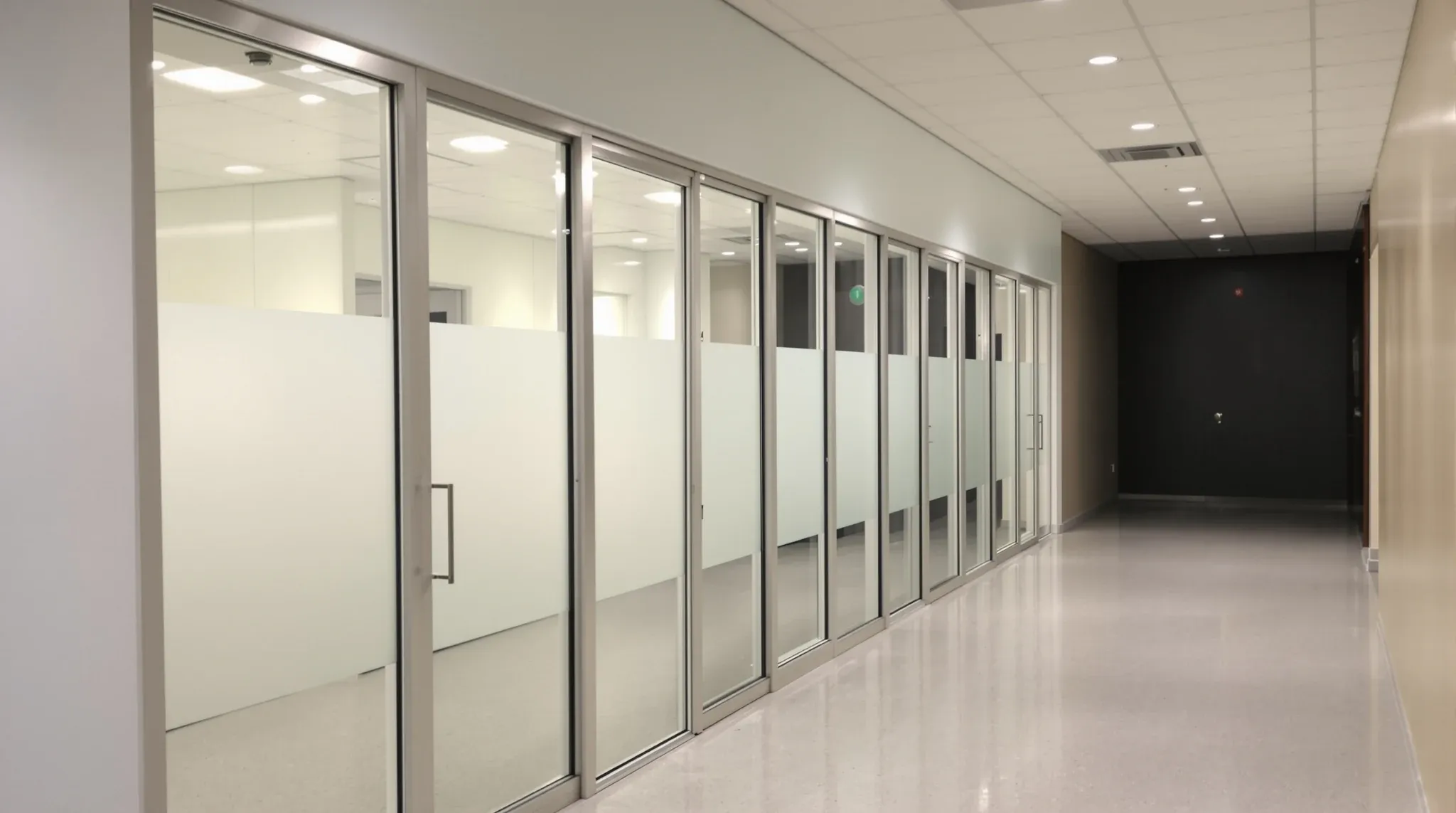 Heavy framed glass consulting room fronts with frosted bands along a medical clinic corridor
