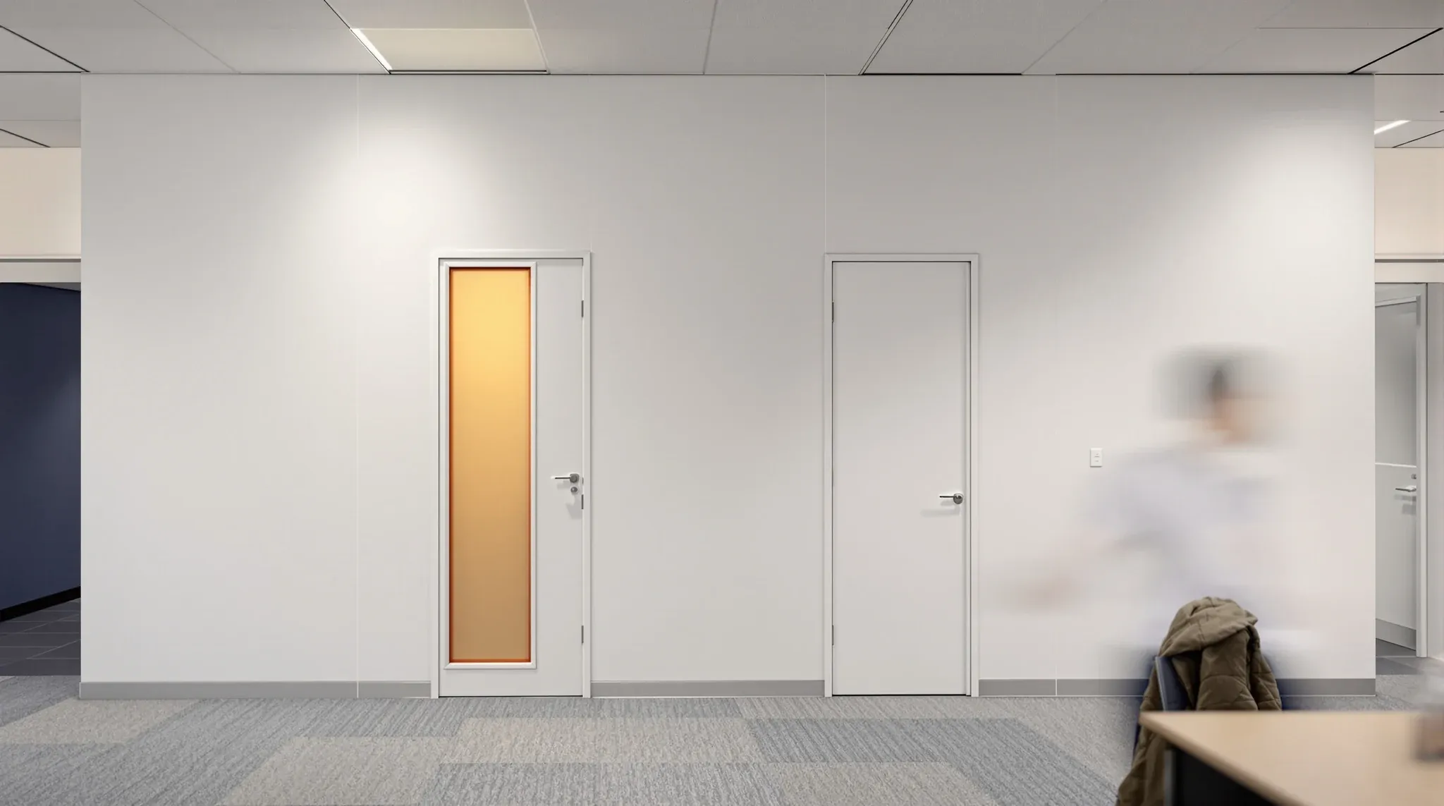A person from behind at a desk against the solid wall of an occupied meeting room