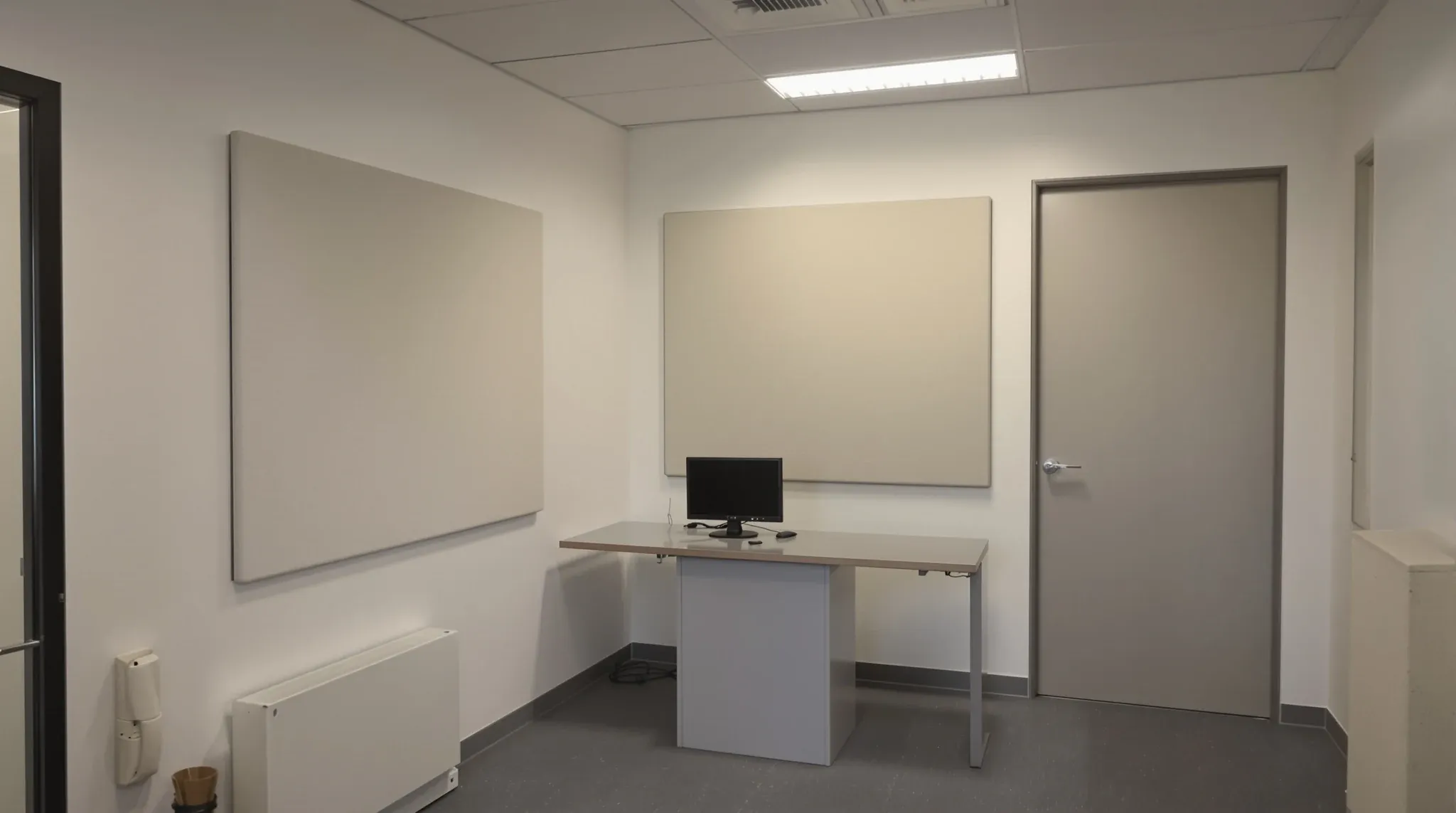 Small finished room with desk, monitor turned off, soft even lighting, acoustic wall panel, closed door