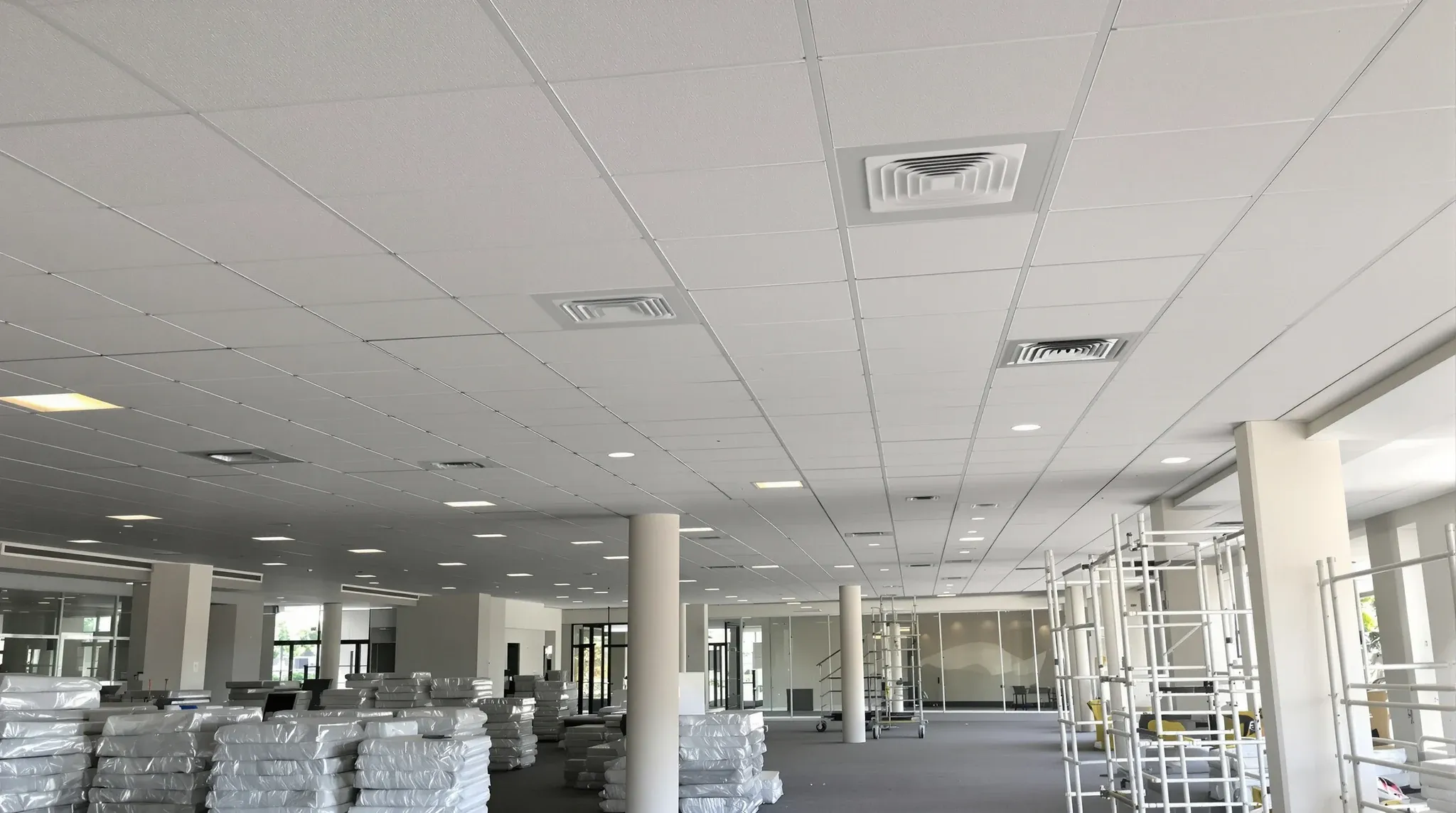 A newly finished suspended ceiling above an empty office floor with spare tiles stacked below