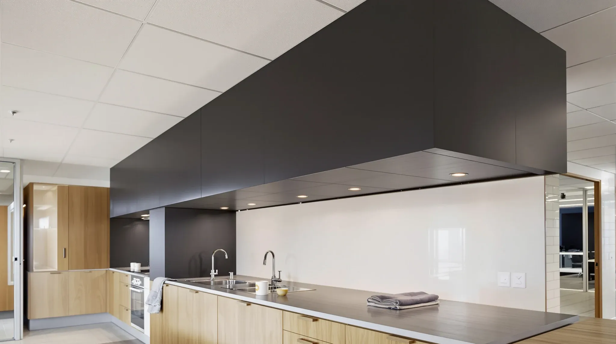 A dark plasterboard bulkhead with warm downlights over an office kitchen bench in the evening