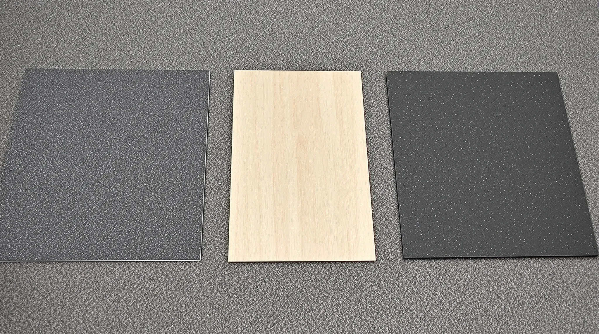 Carpet tile, timber-look vinyl plank and rubber flooring samples laid side by side on an office floor