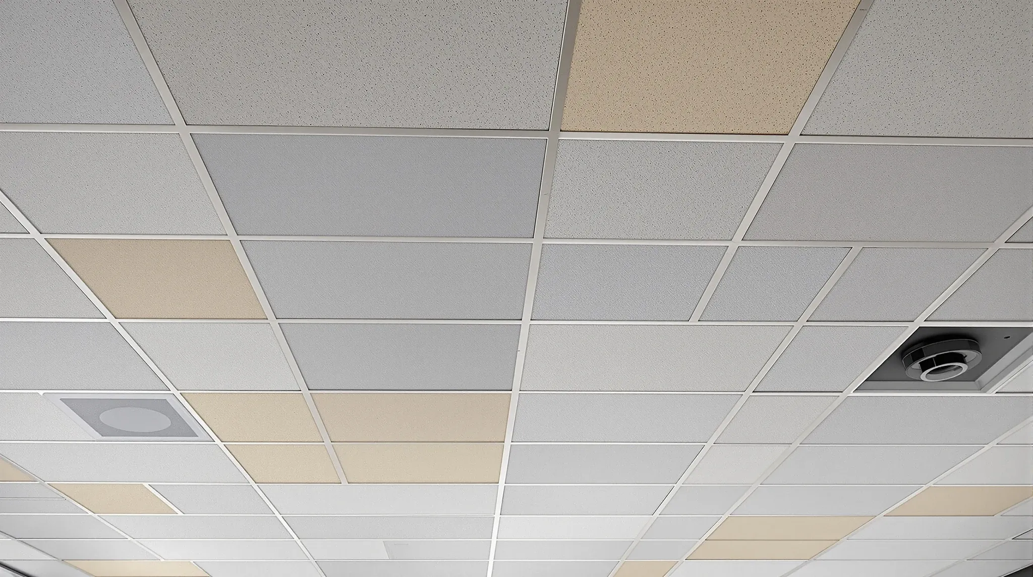 An office ceiling grid with a patchwork of yellowed old tiles and bright new replacement tiles