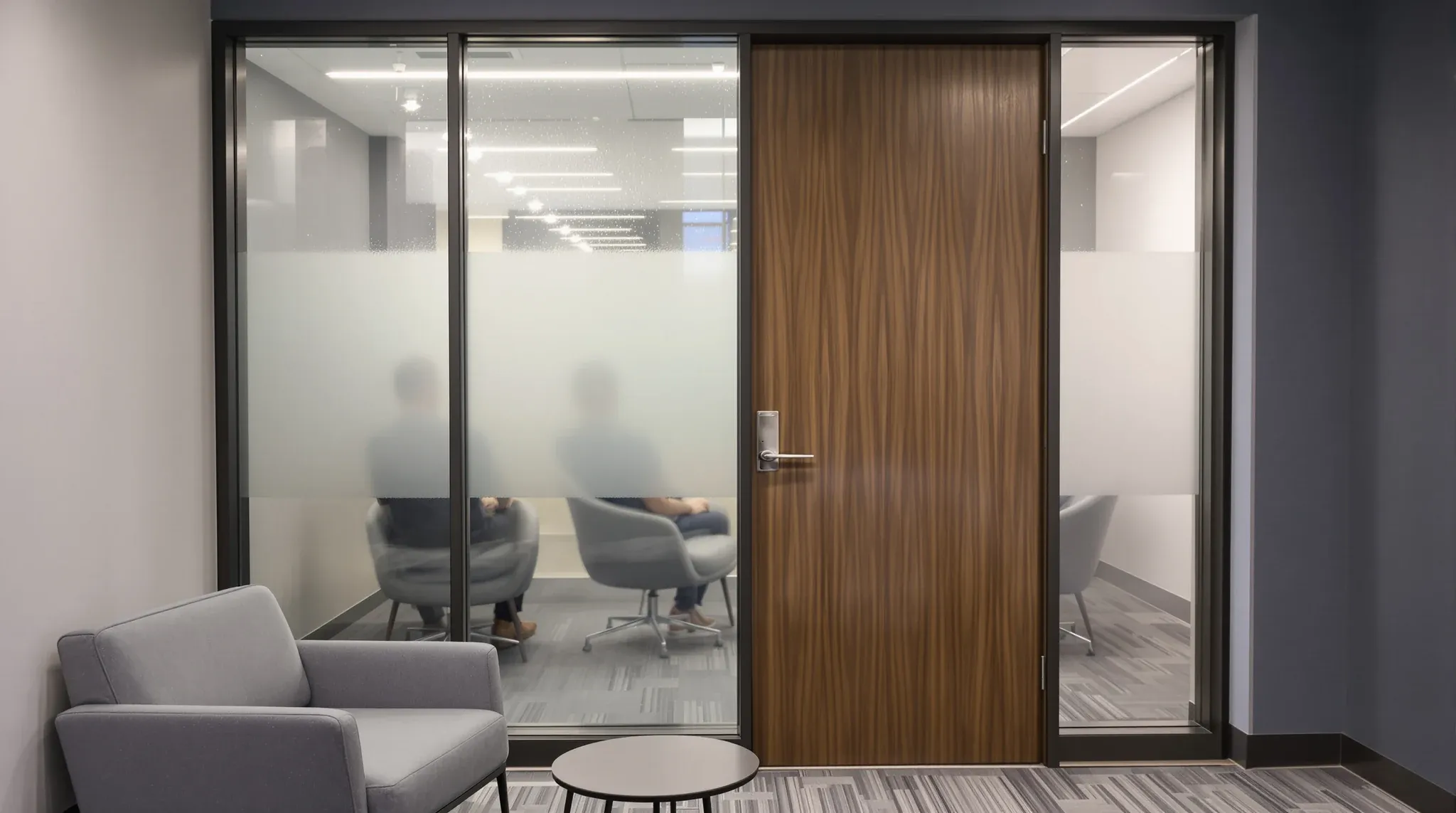 A closed meeting room behind a glass front frosted in a deep band, two seated people blurred behind it