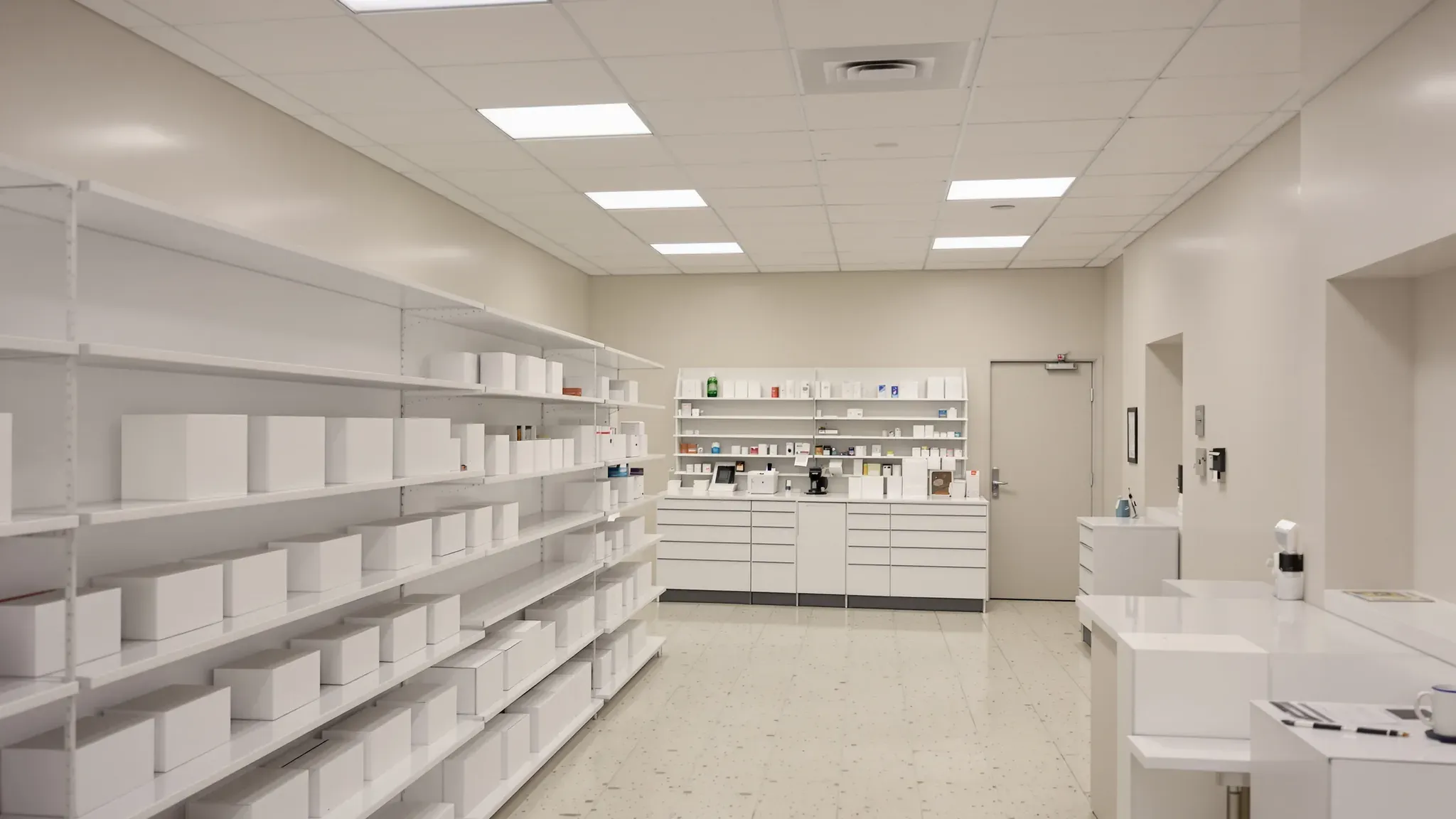 Pharmacy with white shelving down one side and the dispensary counter and shelves at the back