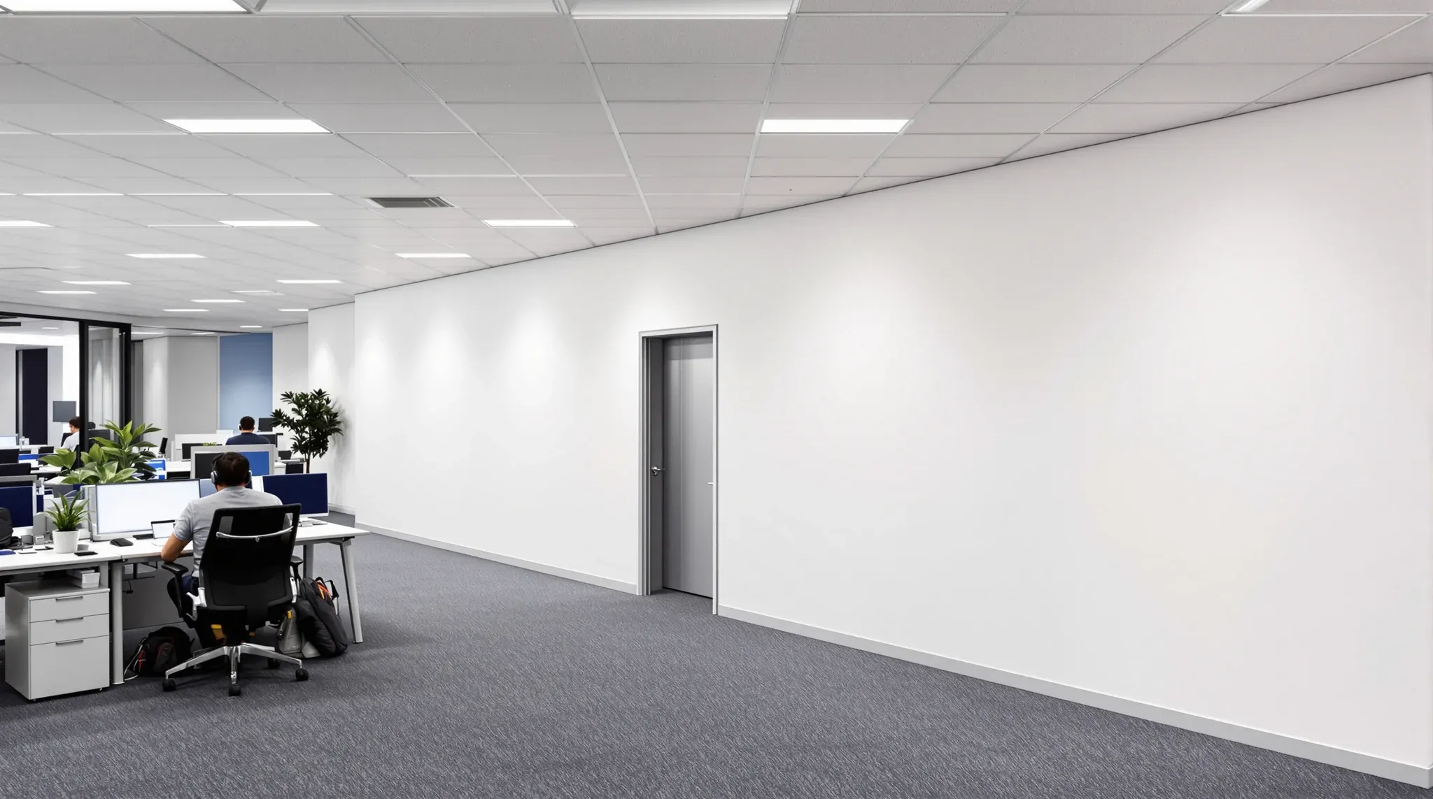Staff at desks beside a plain white full-height hoarding wall with a single door, sealing off works