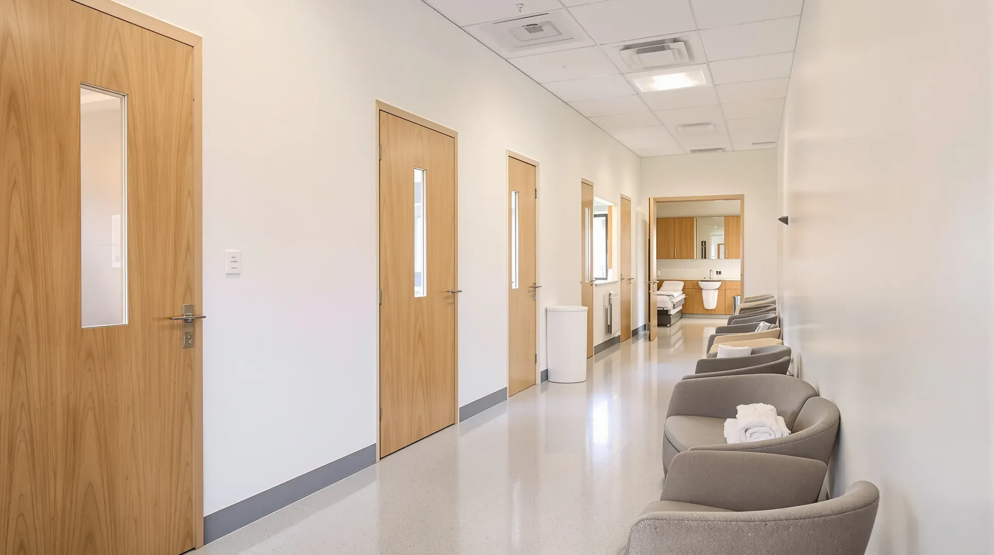 Clinic corridor on a former office floor with timber doors, sheet vinyl floor and a treatment room at the end
