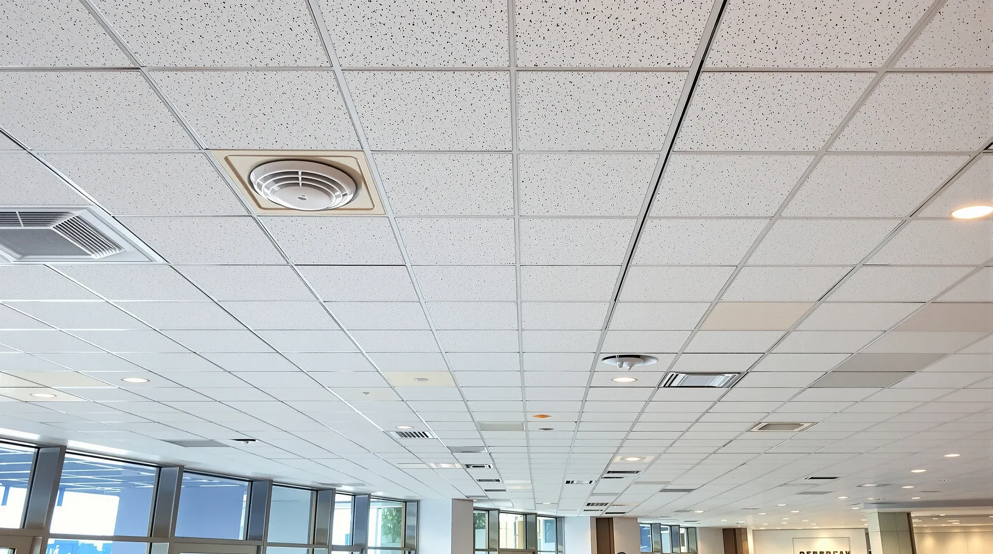 Looking up at an office ceiling grid with lights, diffusers, sprinkler heads and smoke detectors