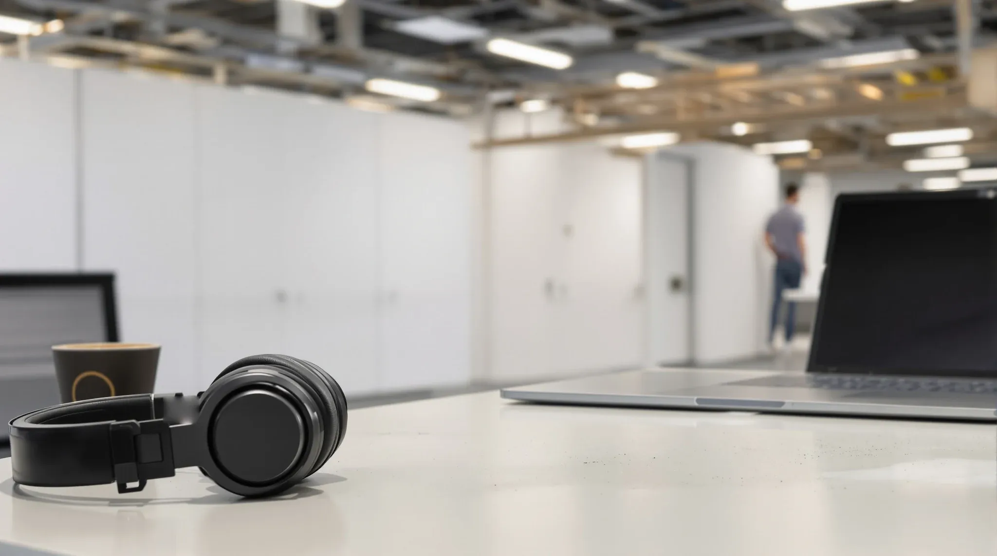 Headphones on a desk, with a temporary wall closing off works blurred in the background